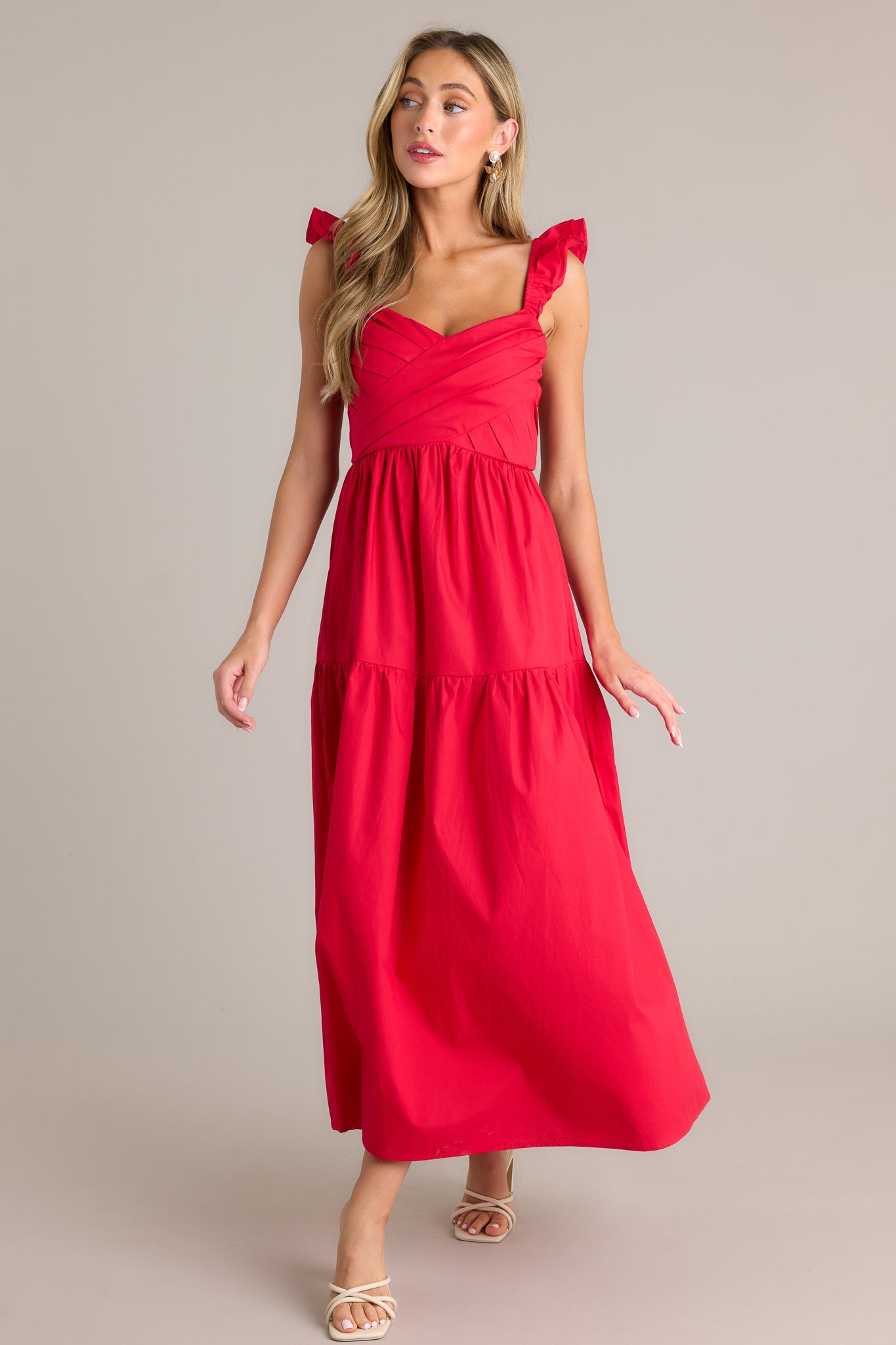 Action shot of a red midi dress displaying the fit and movement, highlighting the v-neckline, pleated bodice, tiered design, layered flutter sleeves, and flowing silhouette.