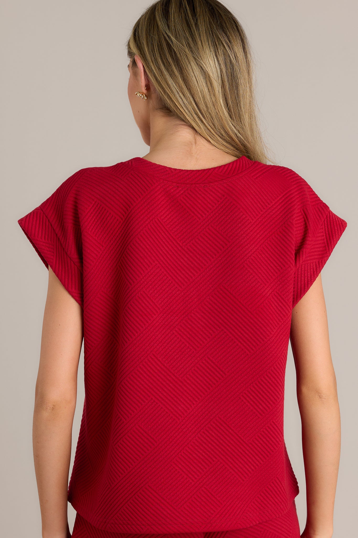 Back view of a scarlet red top highlighting the overall fit, subtle crisscross texturing, and wide cuffed short sleeves