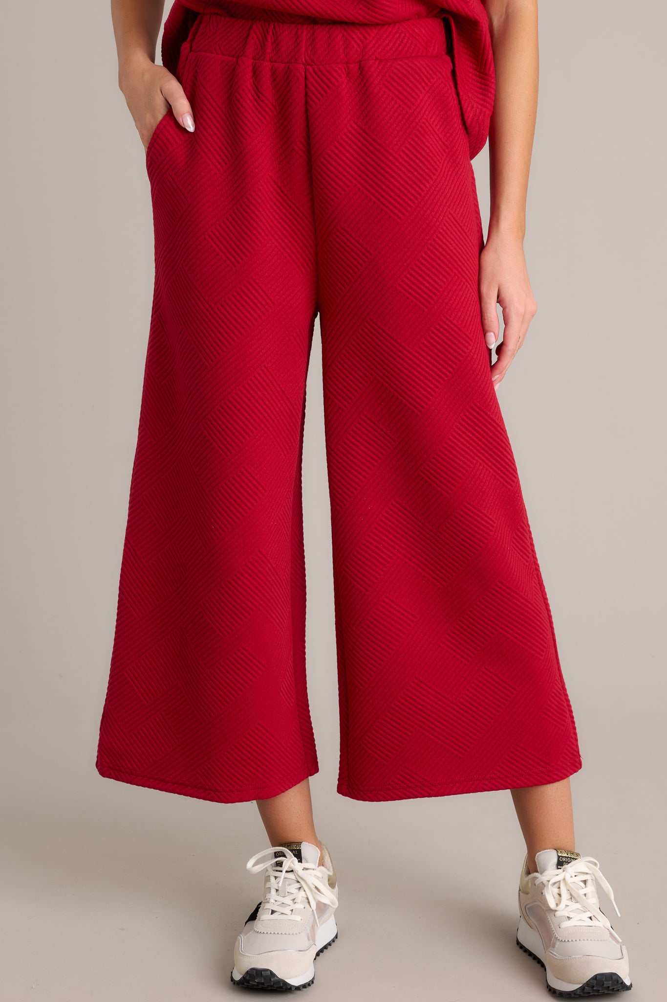 Close-up of red pants highlighting the textured crisscross pattern, elastic waistband, and functional hip pockets with a wide-leg cut.