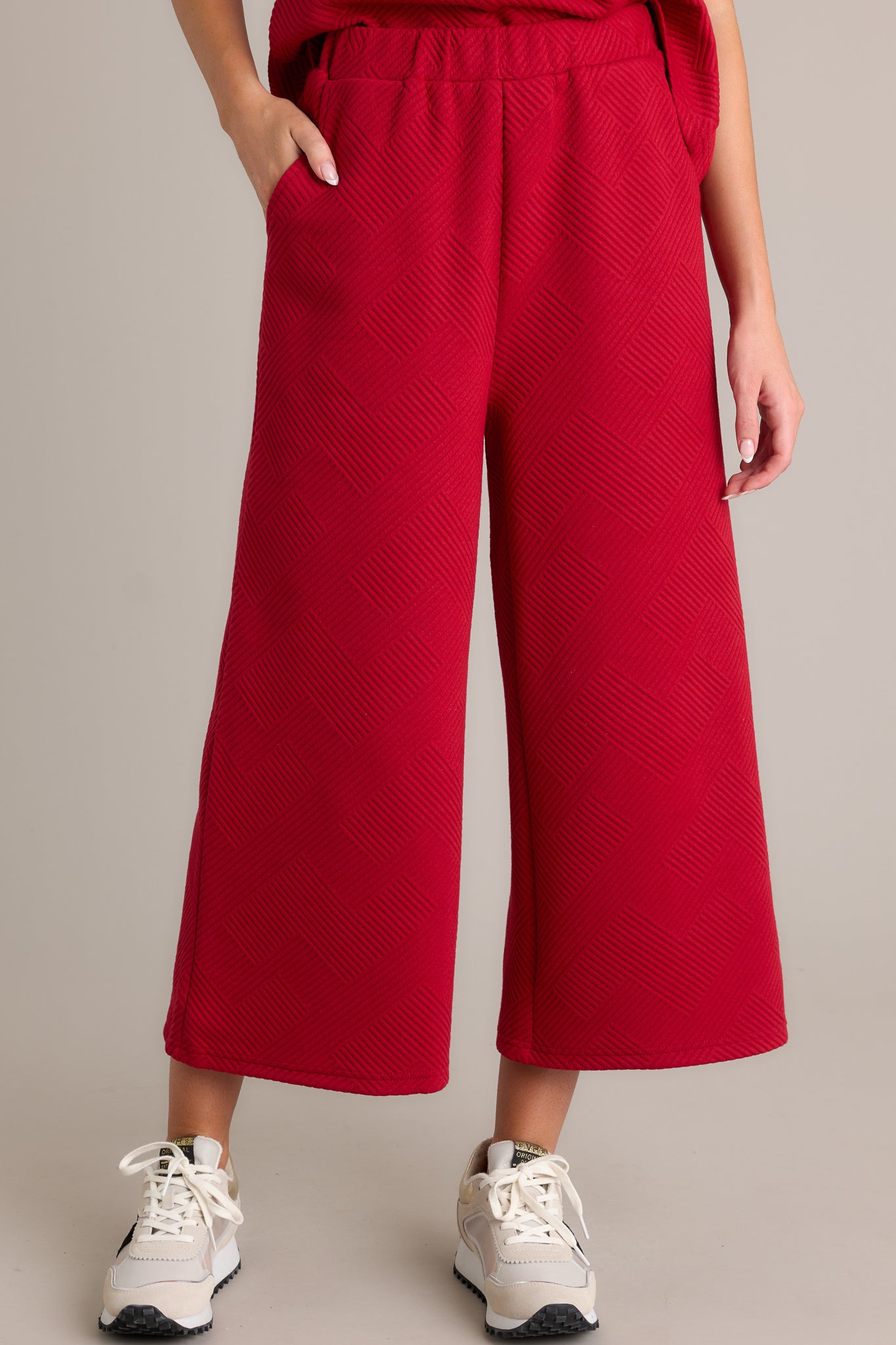 Detailed view of red pants emphasizing the high-waisted design, textured crisscross pattern, elastic waistband, and wide-leg fit.