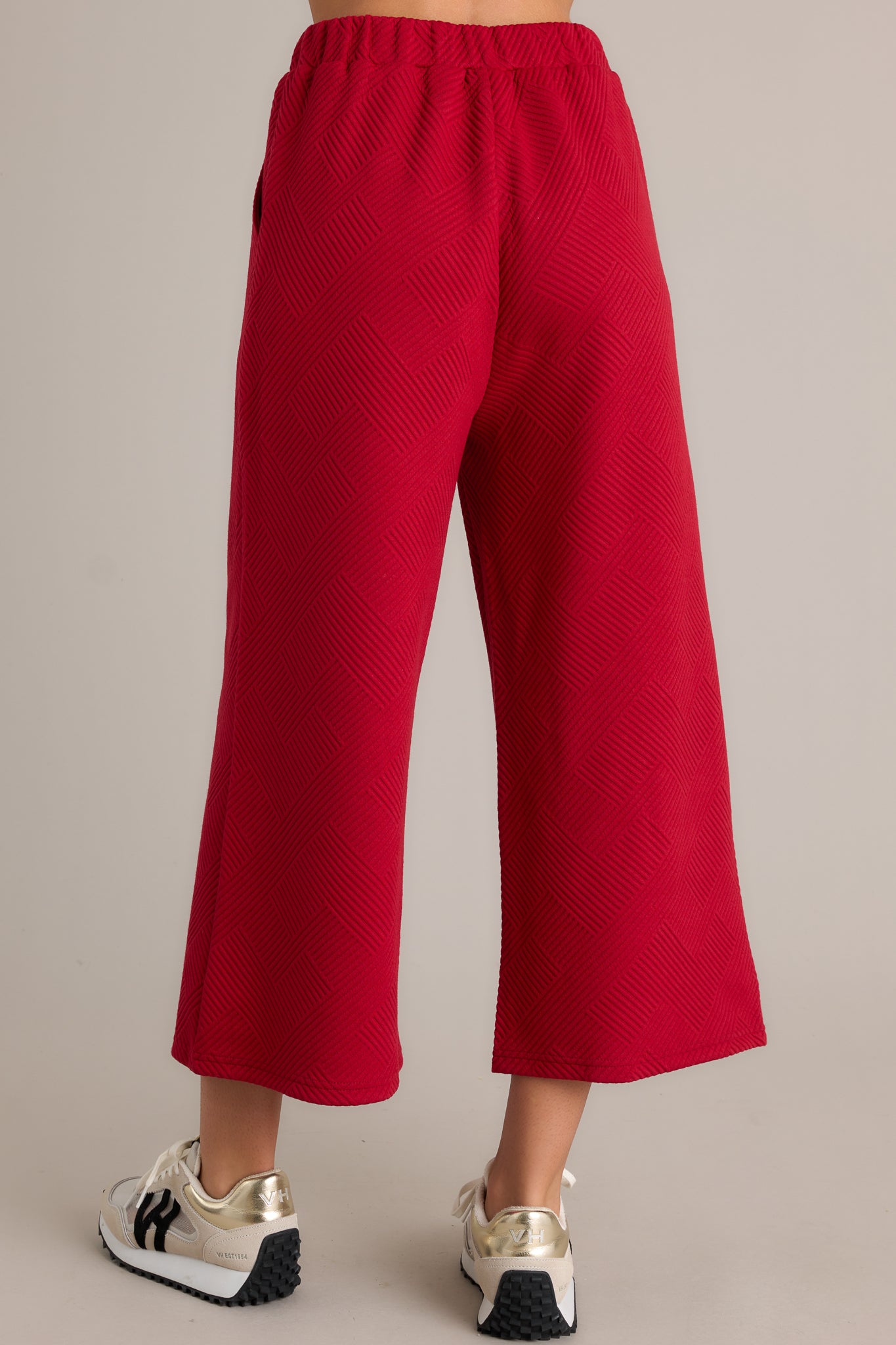 Rear view of red pants with a high-waisted design, elastic waistband, functional hip pockets, and a textured crisscross pattern on a wide-leg cut