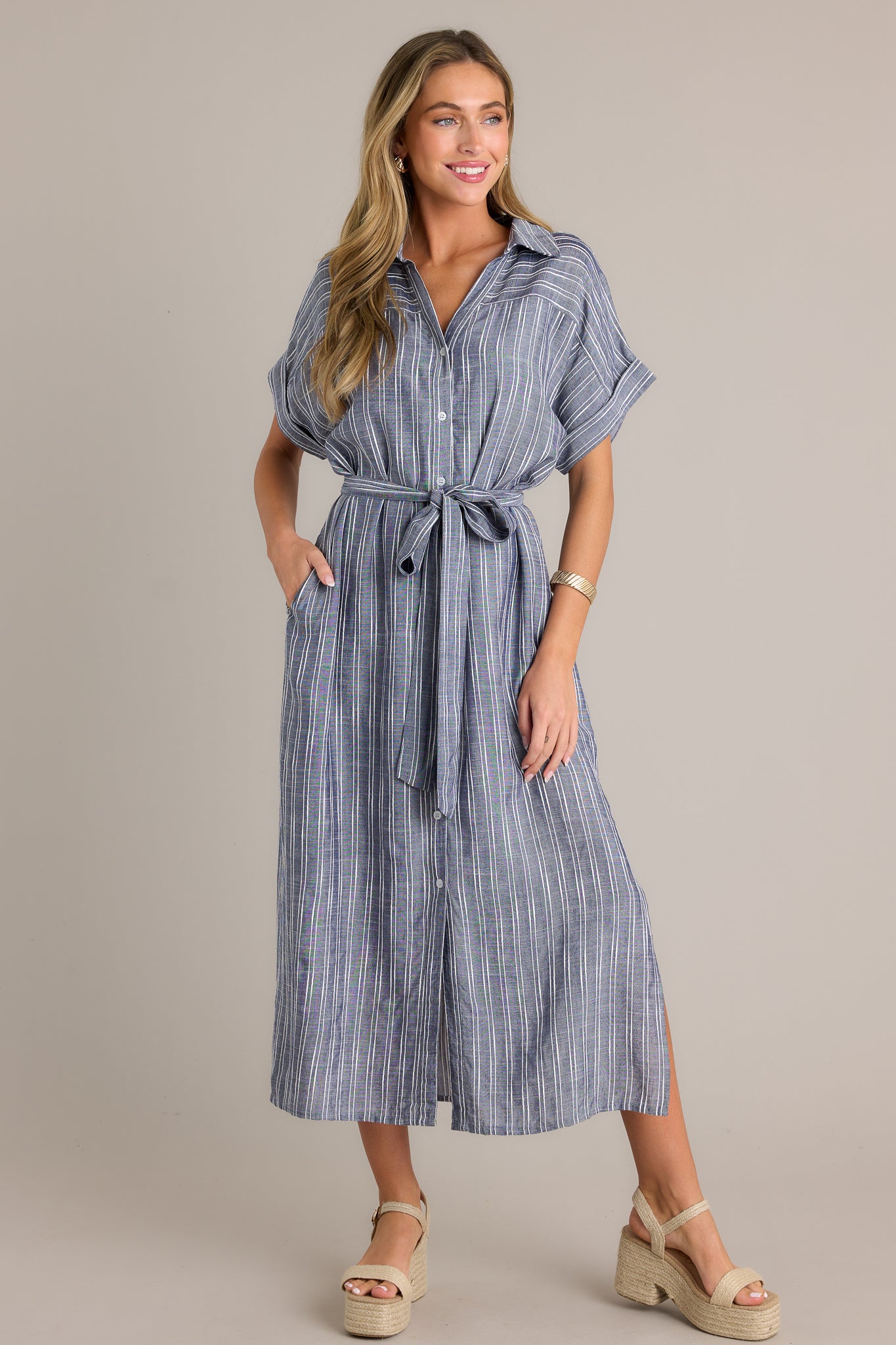 This blue dress features a functional button front, an optional self-tie belt, a collared neckline, and cuffed short sleeves.