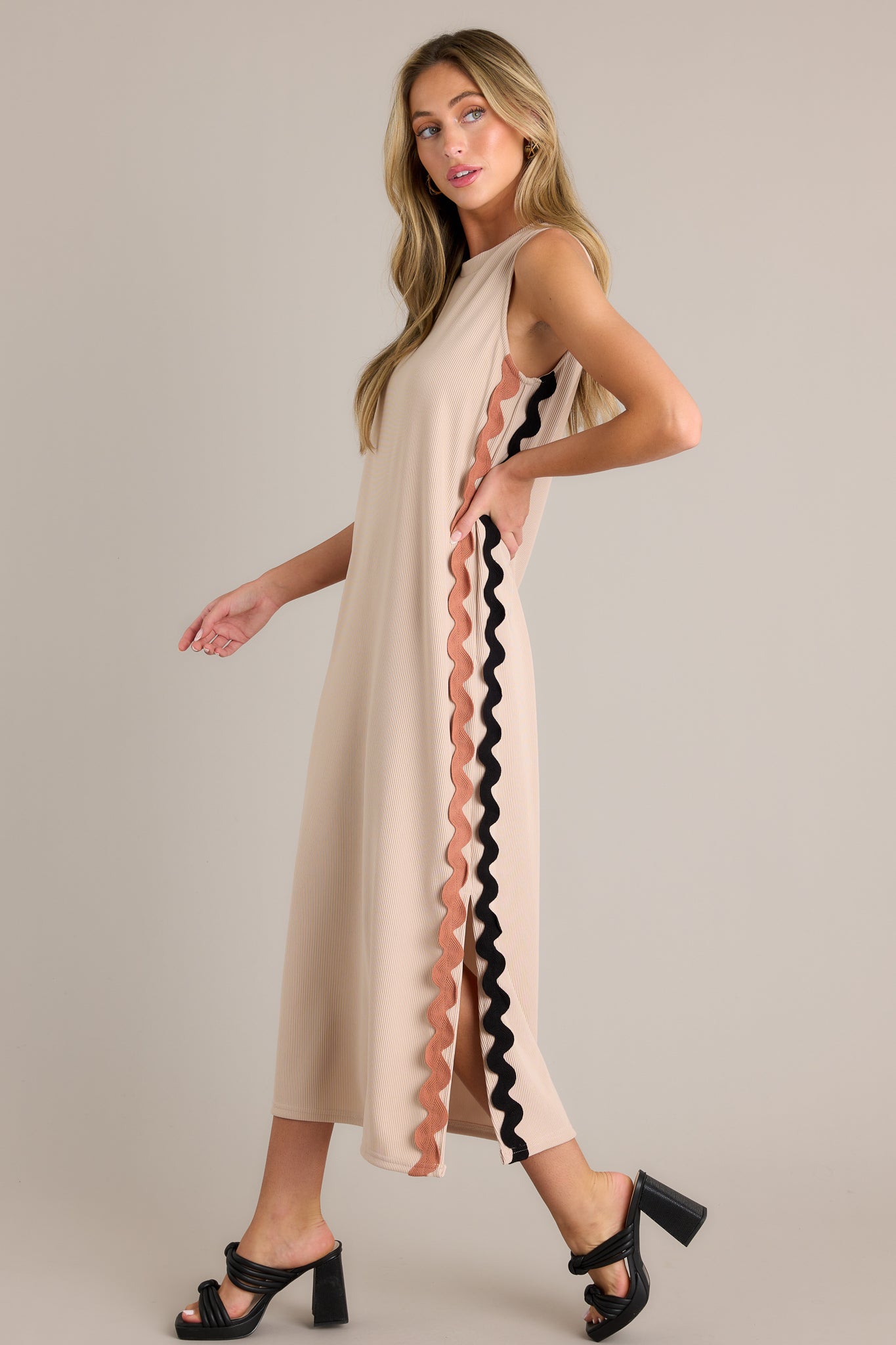 Side view of a taupe midi dress showcasing the crew neckline, ribbed material, two-toned ricrac side detailing, side slits, and sleeveless design.