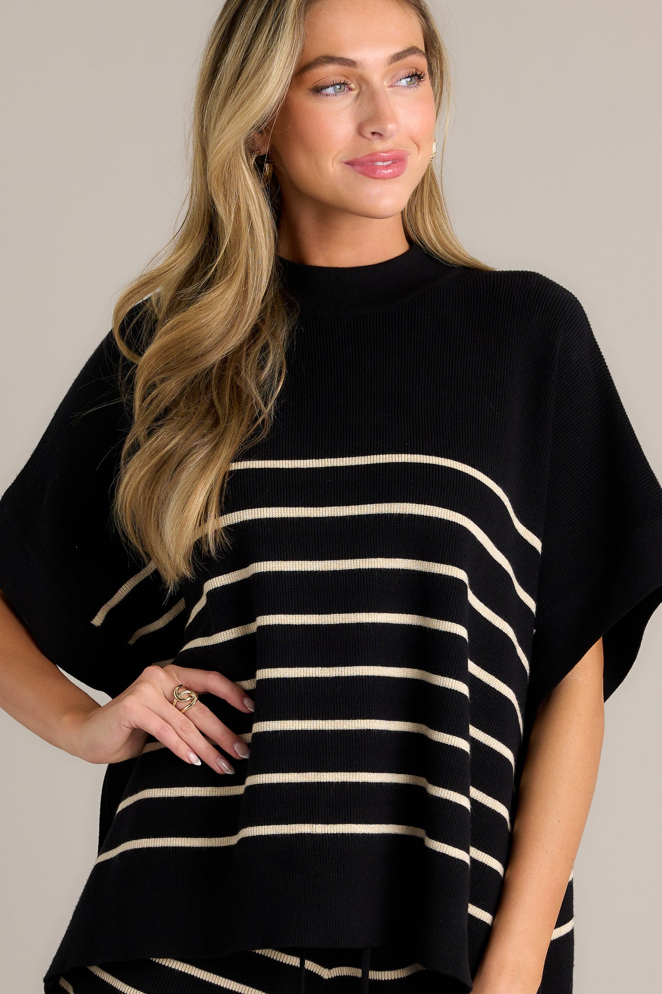 Front view of a stripe poncho top featuring a high neckline, high side slits, a classic stripe design, a thick hem, short sleeves, and an oversized fit.