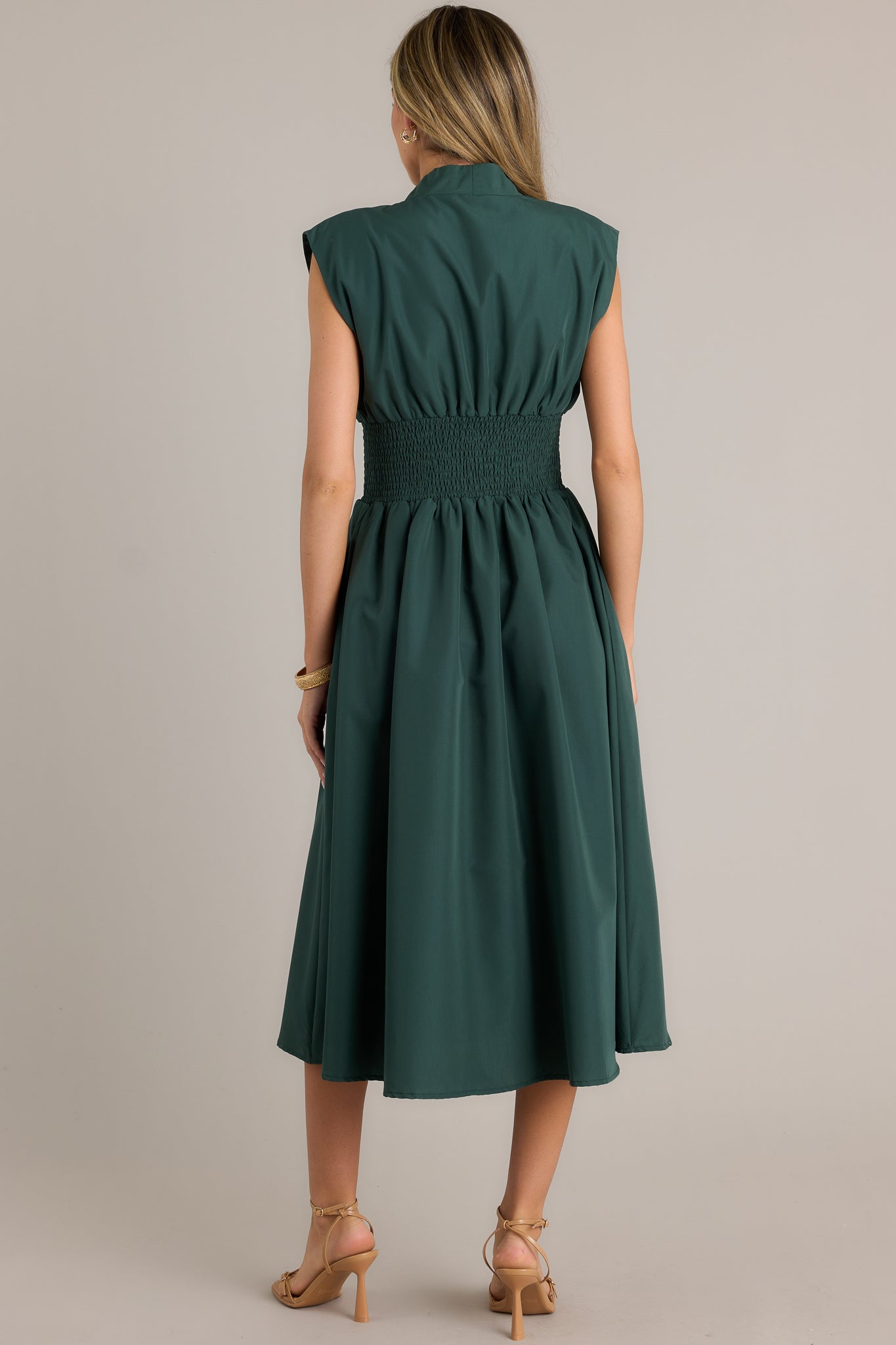 Back view of a hunter green midi dress highlighting the overall fit, padded shoulders, and fully smocked waist.