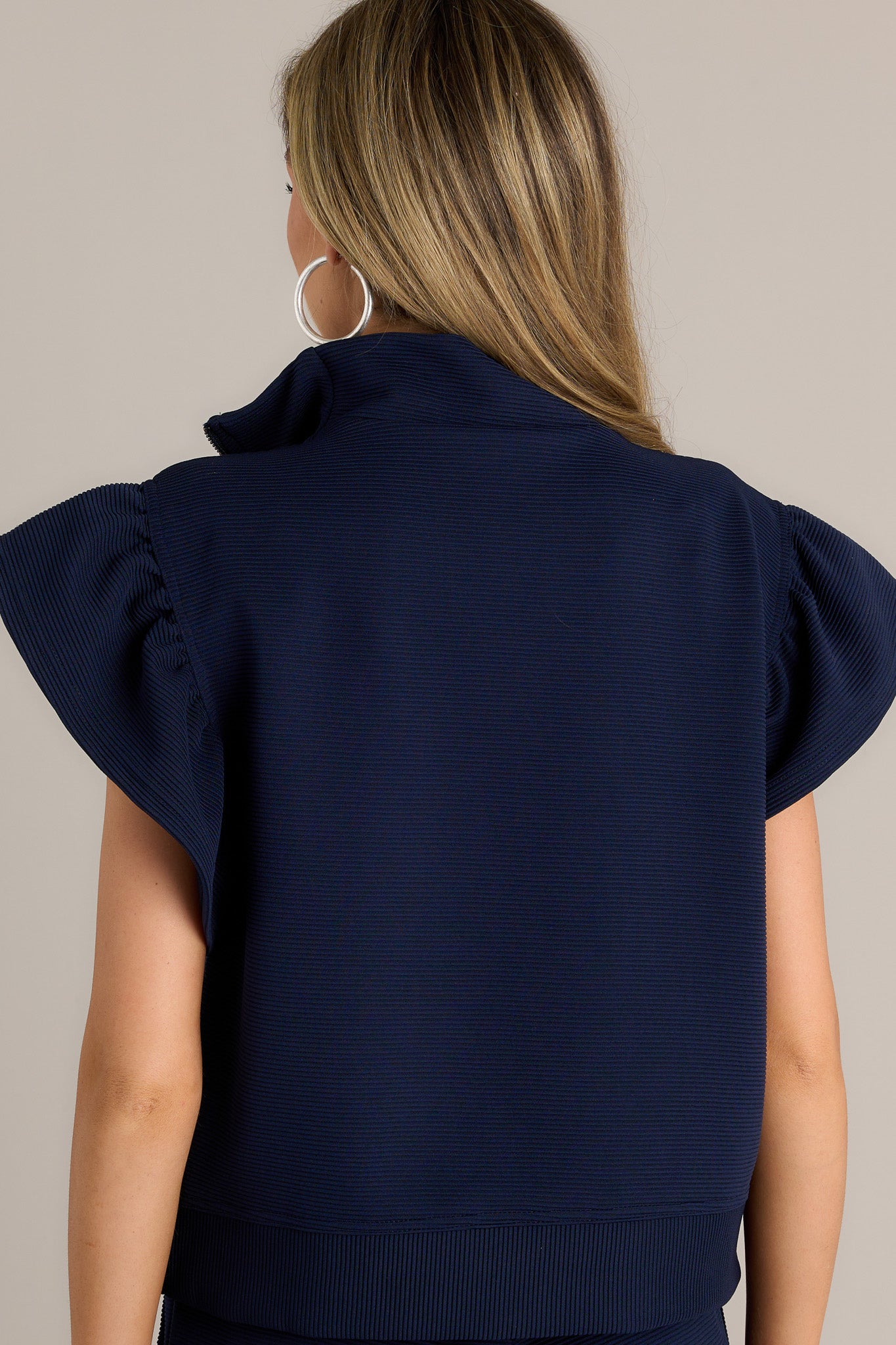 Back view of a navy top highlighting the overall fit, ribbed fabric, and wide ruffled sleeves..