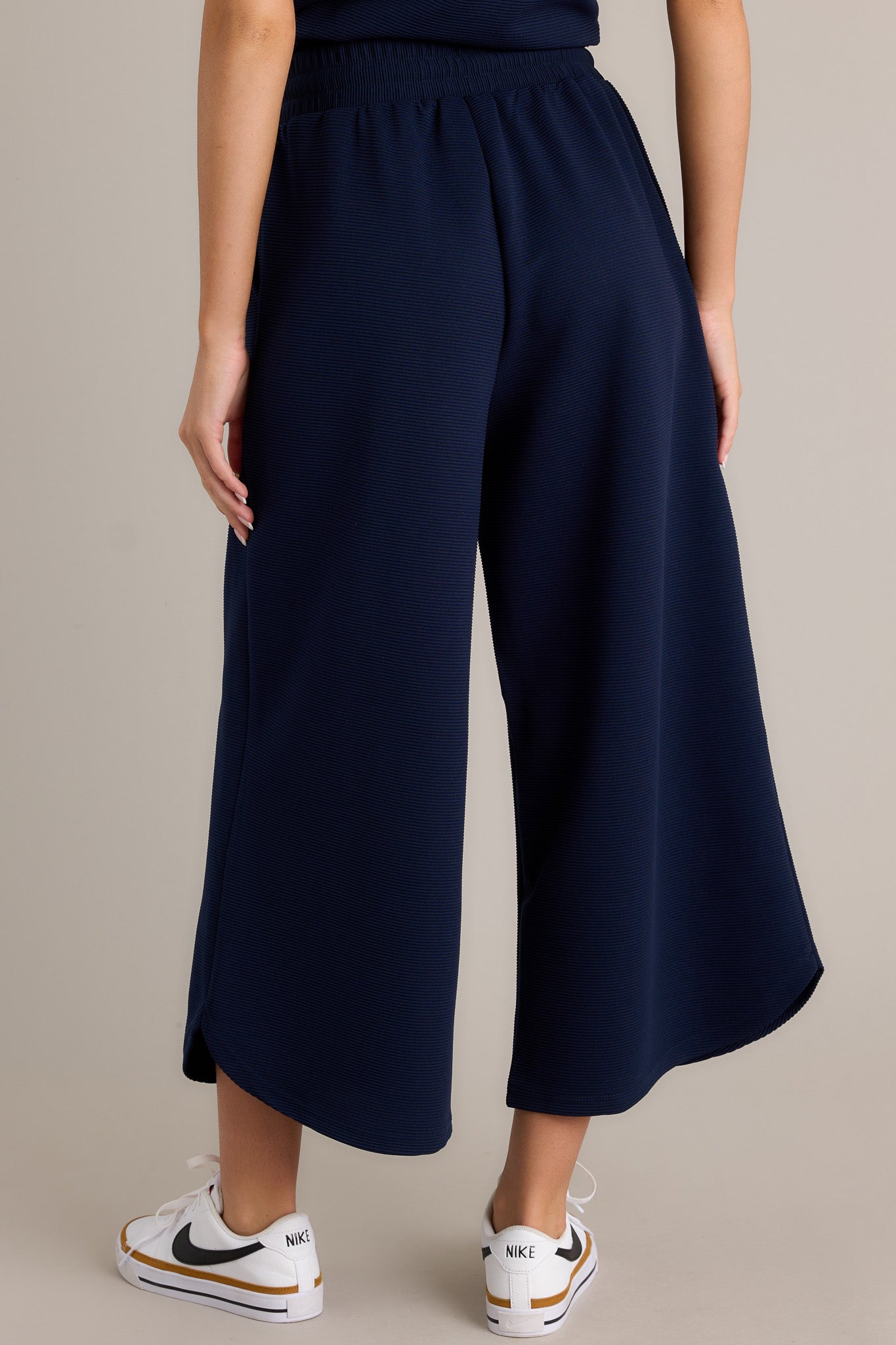 Back view of navy pants highlighting the overall fit, ribbed texture, wide leg, and scooped hemline.