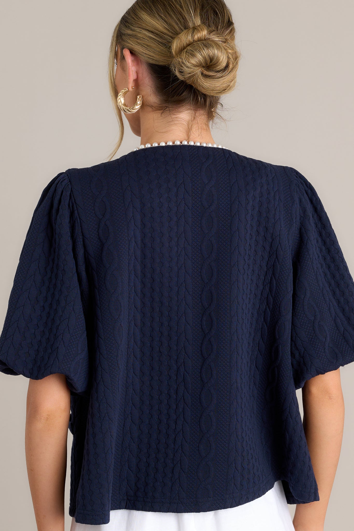 Back view of a navy short sleeve jacket highlighting the overall fit, quilted design, and elastic cuffed puff sleeves.