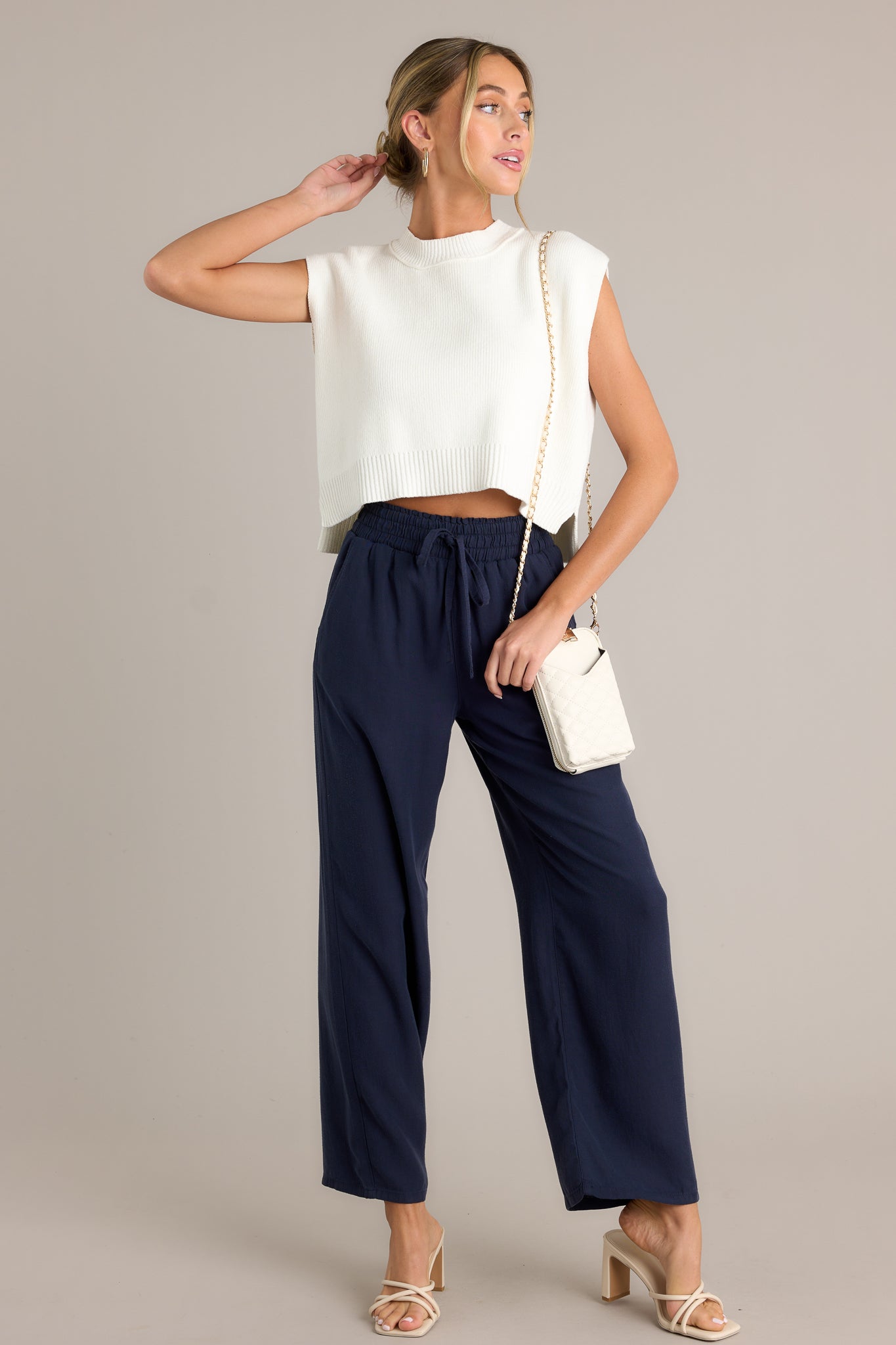 Full body view of the material of these navy pants that feature a high waisted design, an elastic waistband with a self-tie drawstring, functional front & back pockets, and a wide leg.