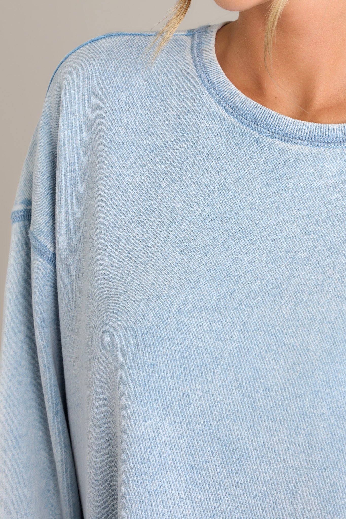 Close up view of this weekender that features a crew neckline, dropped shoulders, exposed seams, and a split ribbed hemline.