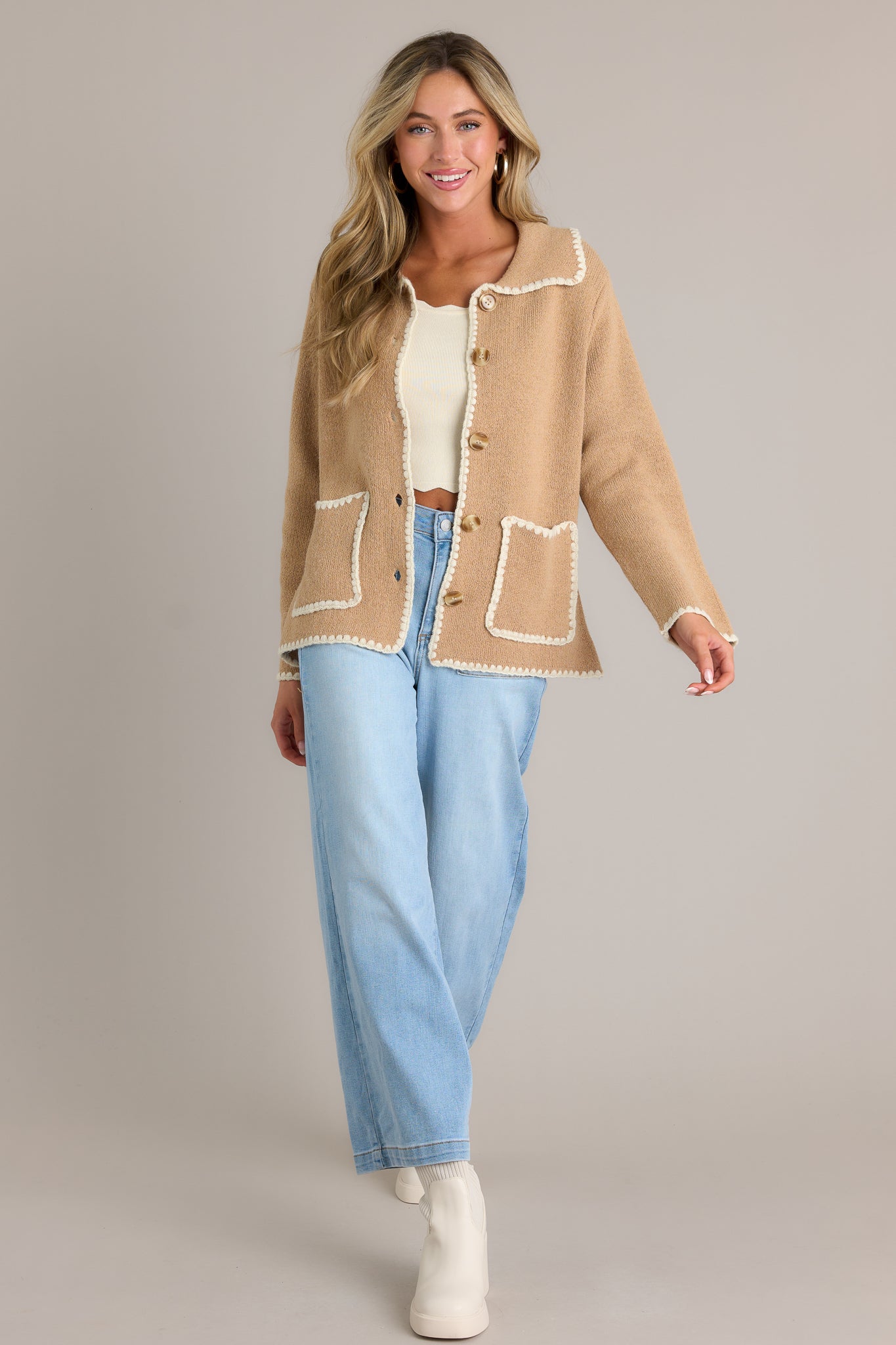 Full length view of a tan jacket with a collared neckline, a full button front, functional pockets, and ivory knitted trim