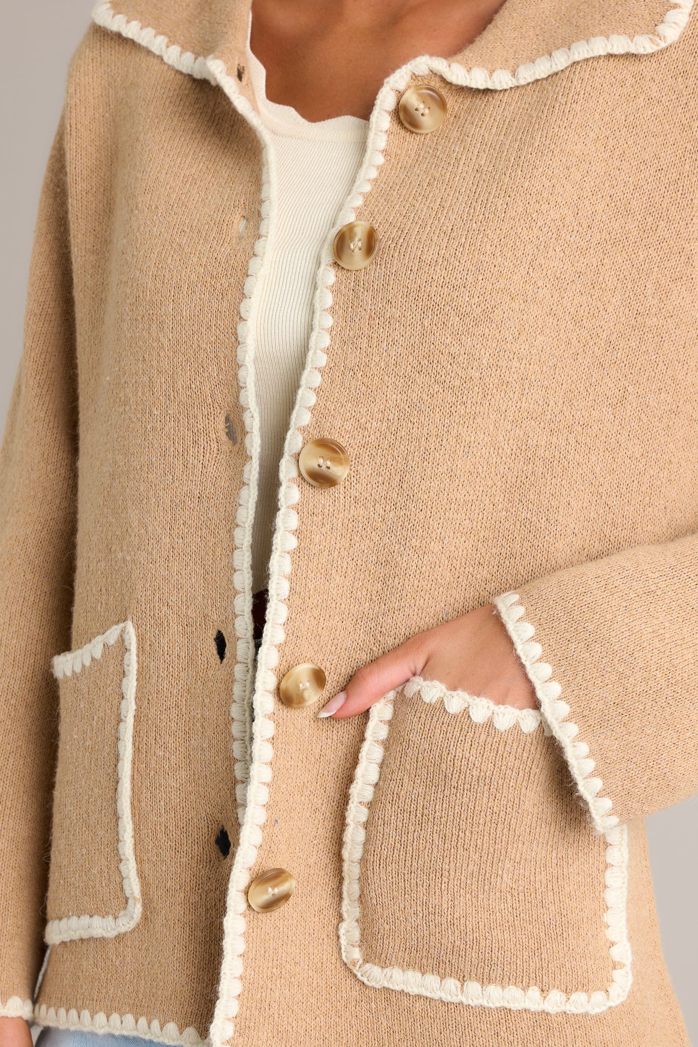 Close-up of the tan jacket showing the collared neckline, full button front, functional pockets, and ivory knitted trim