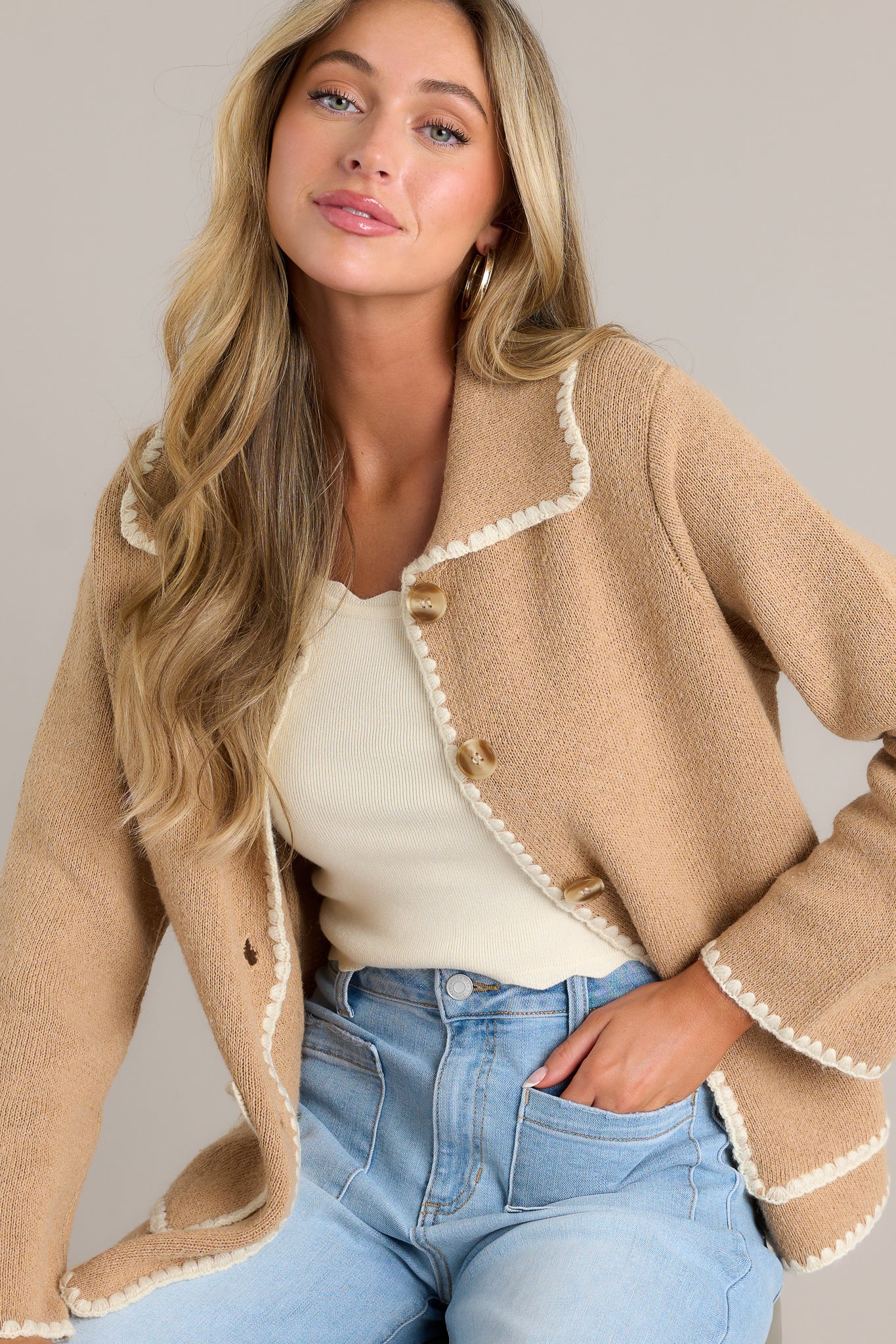 This tan jacket features a collared neckline, a full button front, functional pockets, and ivory knitted trim.