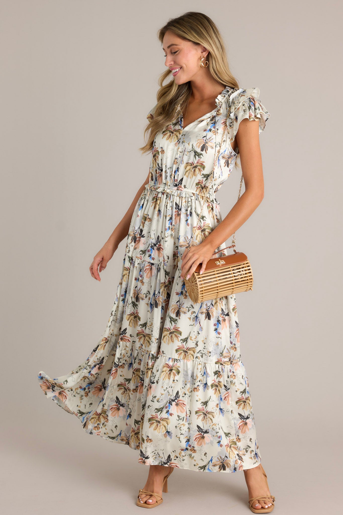 Side view of an ivory floral dress showcasing the v-neckline, self-tie drawstring, floral pattern, tiered design, tiered sleeves, and flowing silhouette.