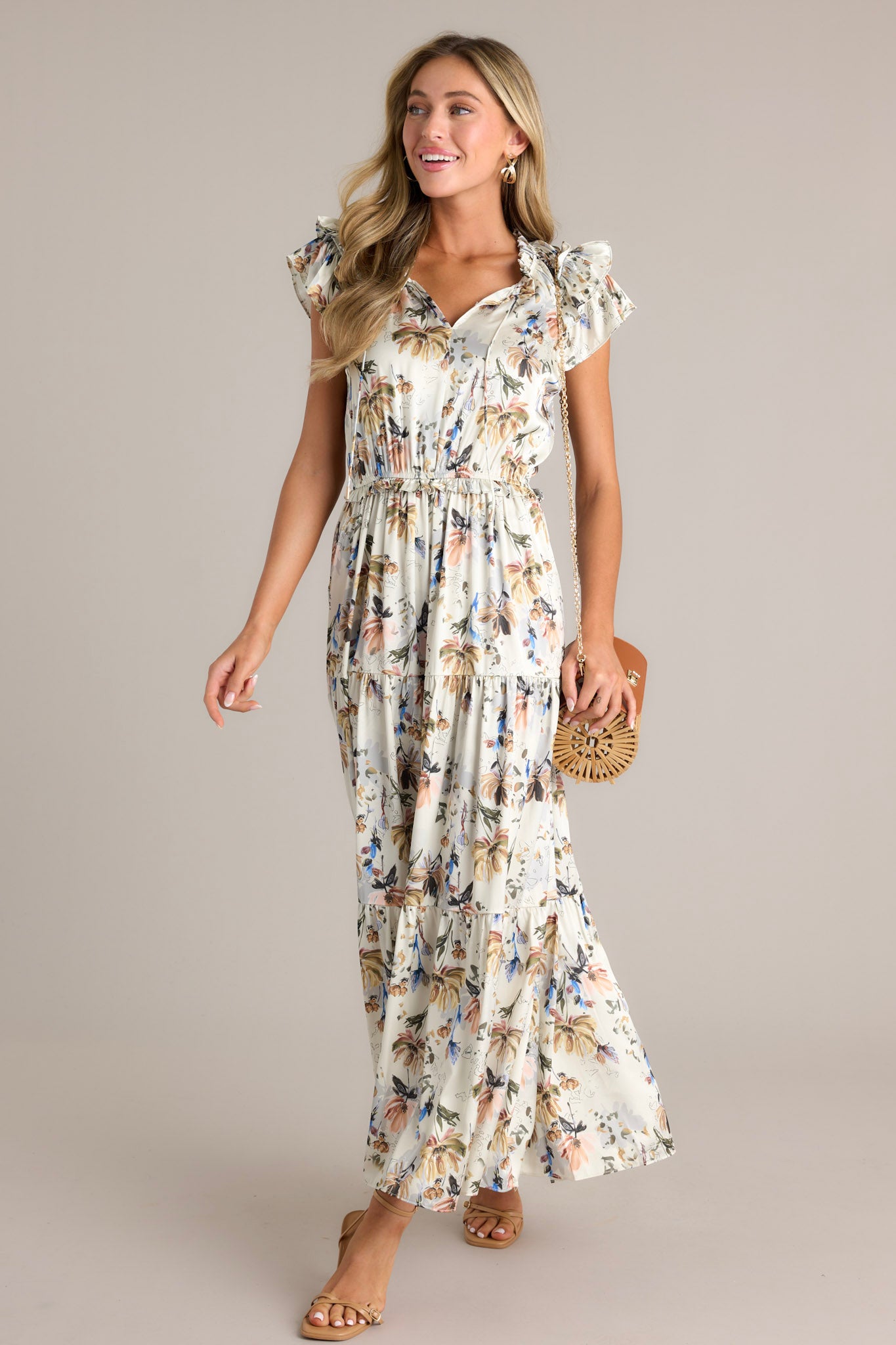 Front angled view of an ivory floral dress featuring a v-neckline, a self-tie drawstring, a floral pattern, a tiered design, tiered sleeves, and a flowing silhouette