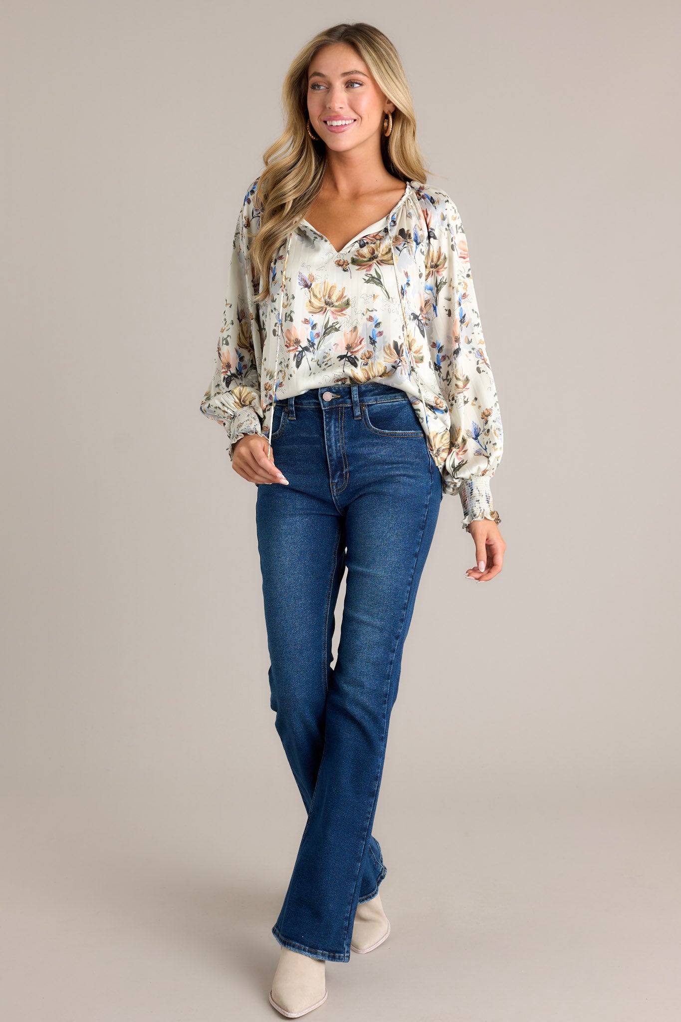 Action shot of an ivory floral blouse displaying the fit and movement, highlighting the v-neckline with self-tie drawstring, lined bodice, balloon sleeves with smocked cuffs, and pleated design.