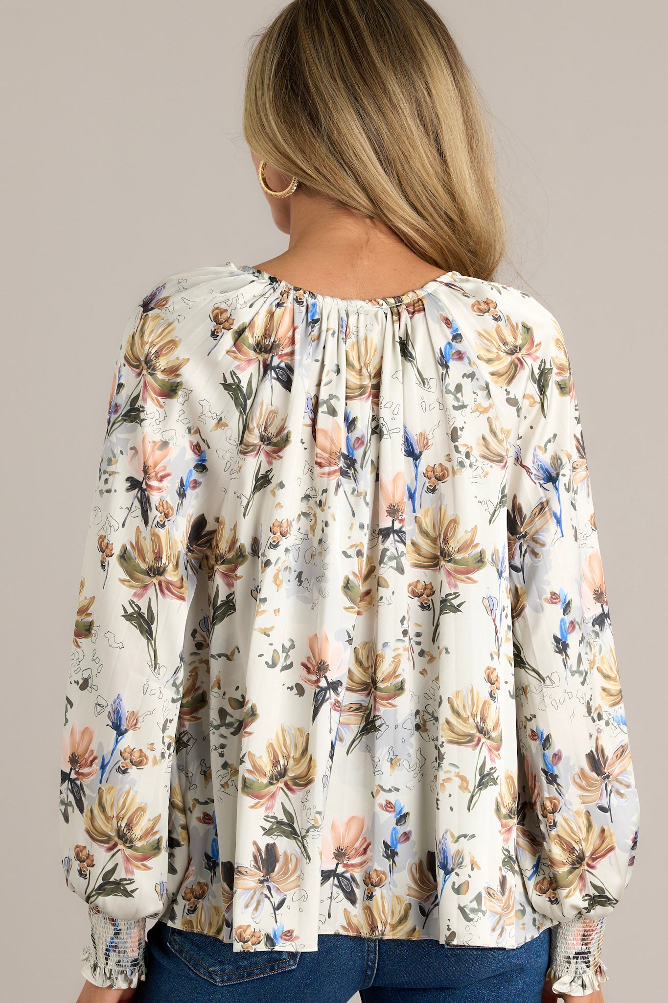 Back view of an ivory floral blouse highlighting the overall fit, balloon sleeves with smocked cuffs, and pleated design.