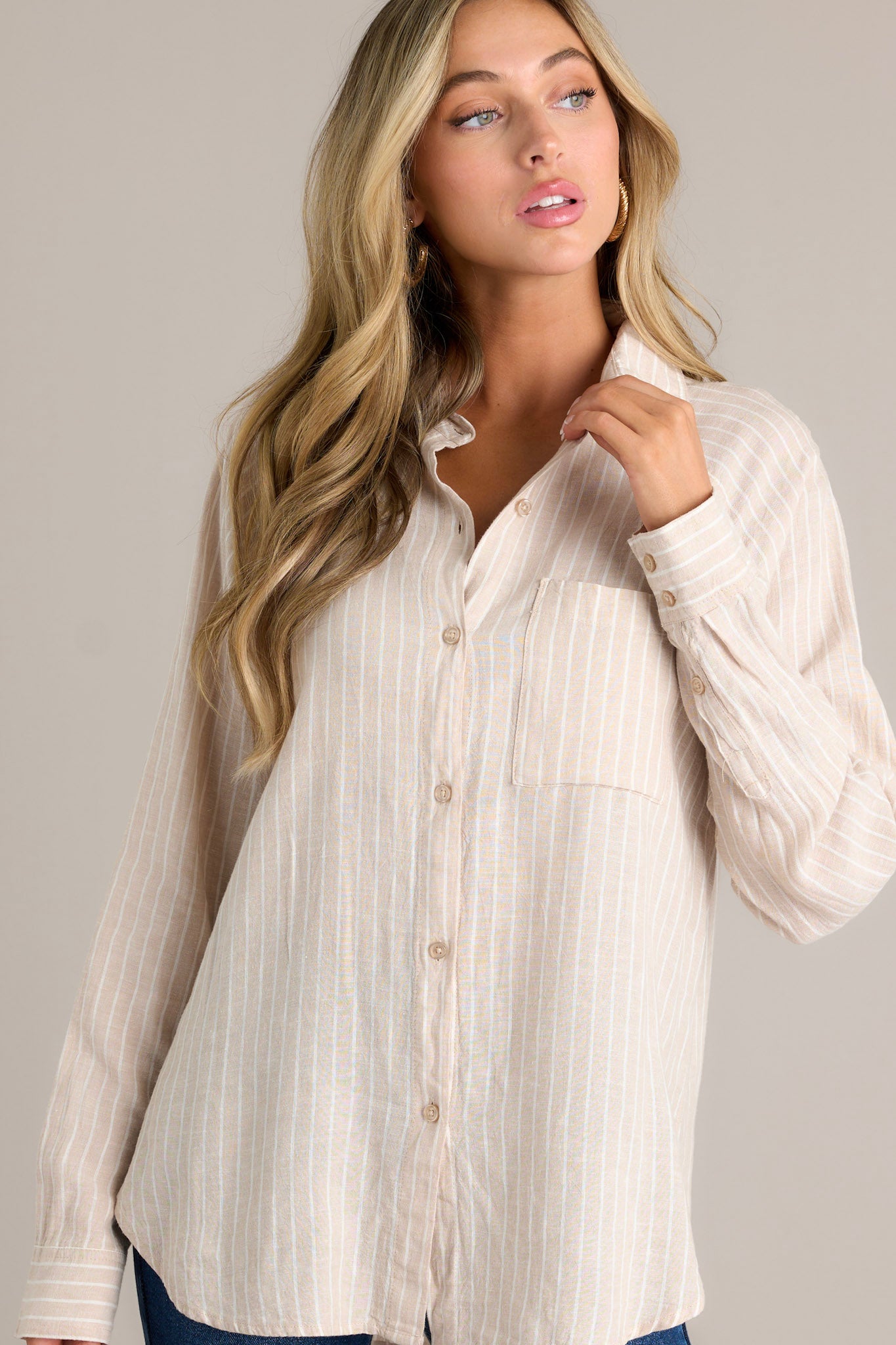 Side view of a beige stripe top showcasing the collared neckline, functional button front, breast pocket, button cuffed long sleeves, and split high low hemline.