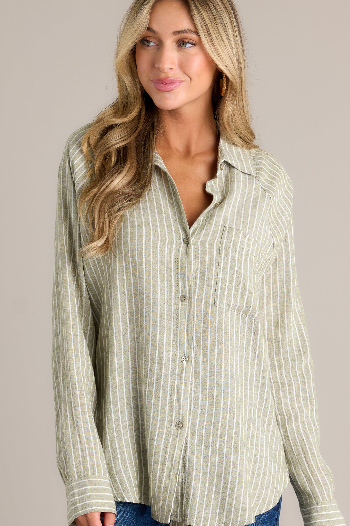 Front angled view of a green stripe top featuring a collared neckline, a functional button front, a breast pocket, button cuffed long sleeves, and a split high low hemline