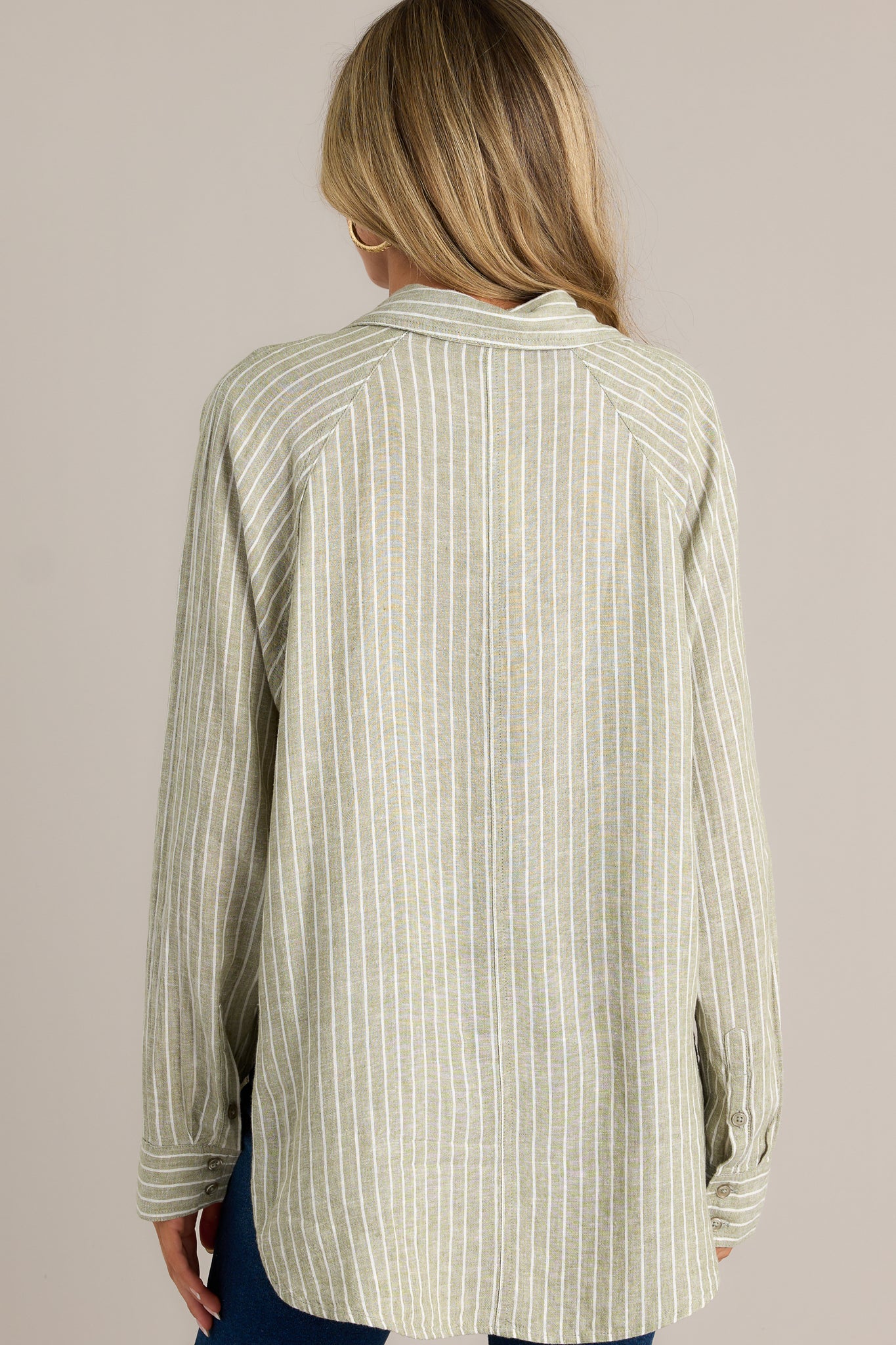 Back view of a green stripe top highlighting the overall fit, button cuffed long sleeves, and split high low hemline.