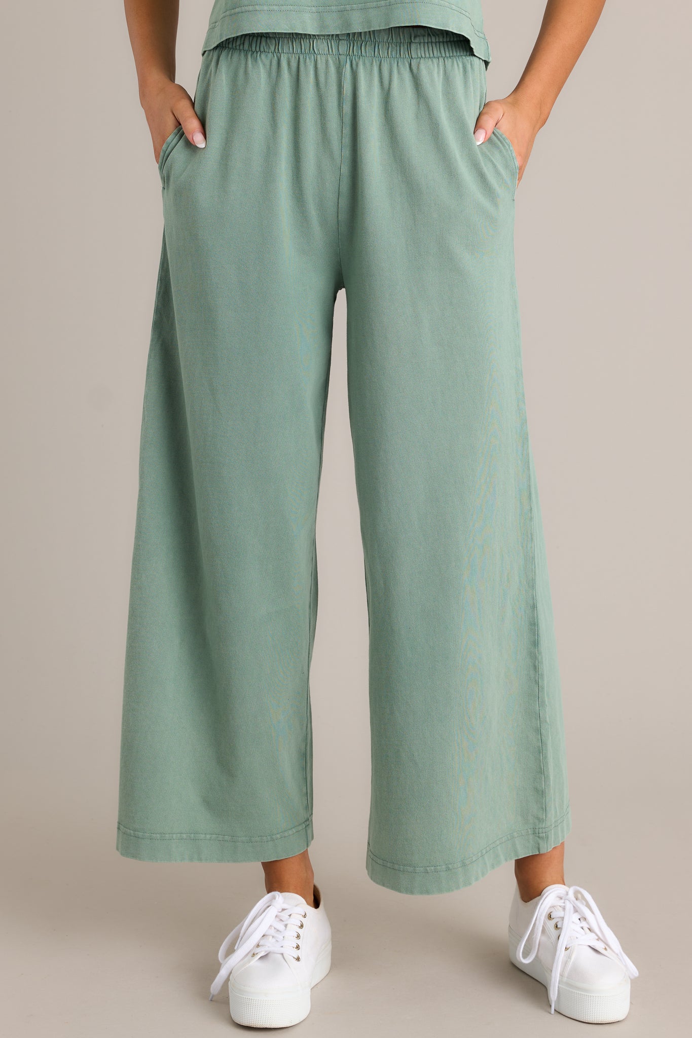 Front view of green flare pants featuring an elastic waistband, functional pockets, a wide leg design, and a soft jersey material.