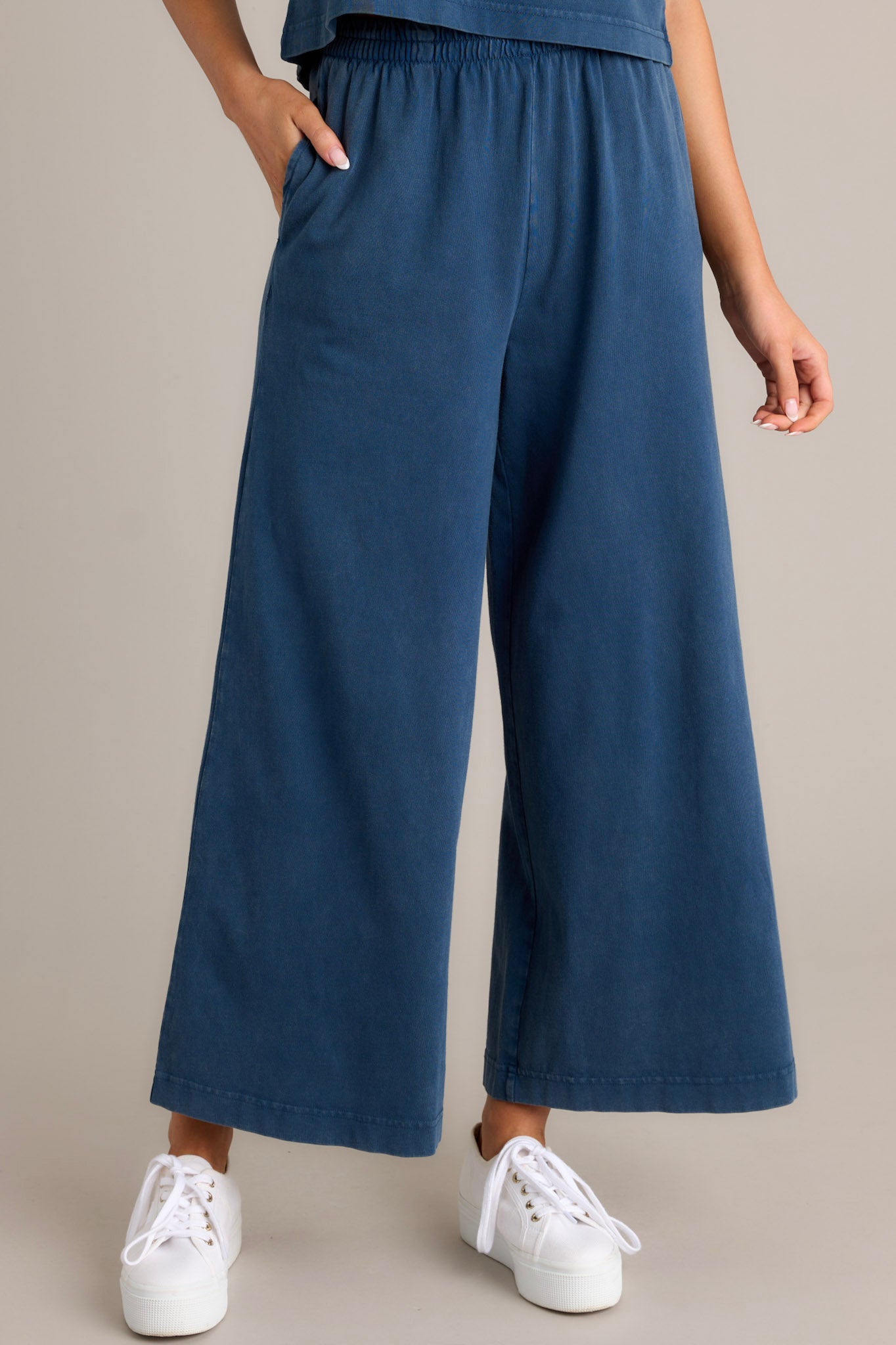 Front view of blue flare pants featuring an elastic waistband, functional pockets, a wide leg design, and a soft jersey material.