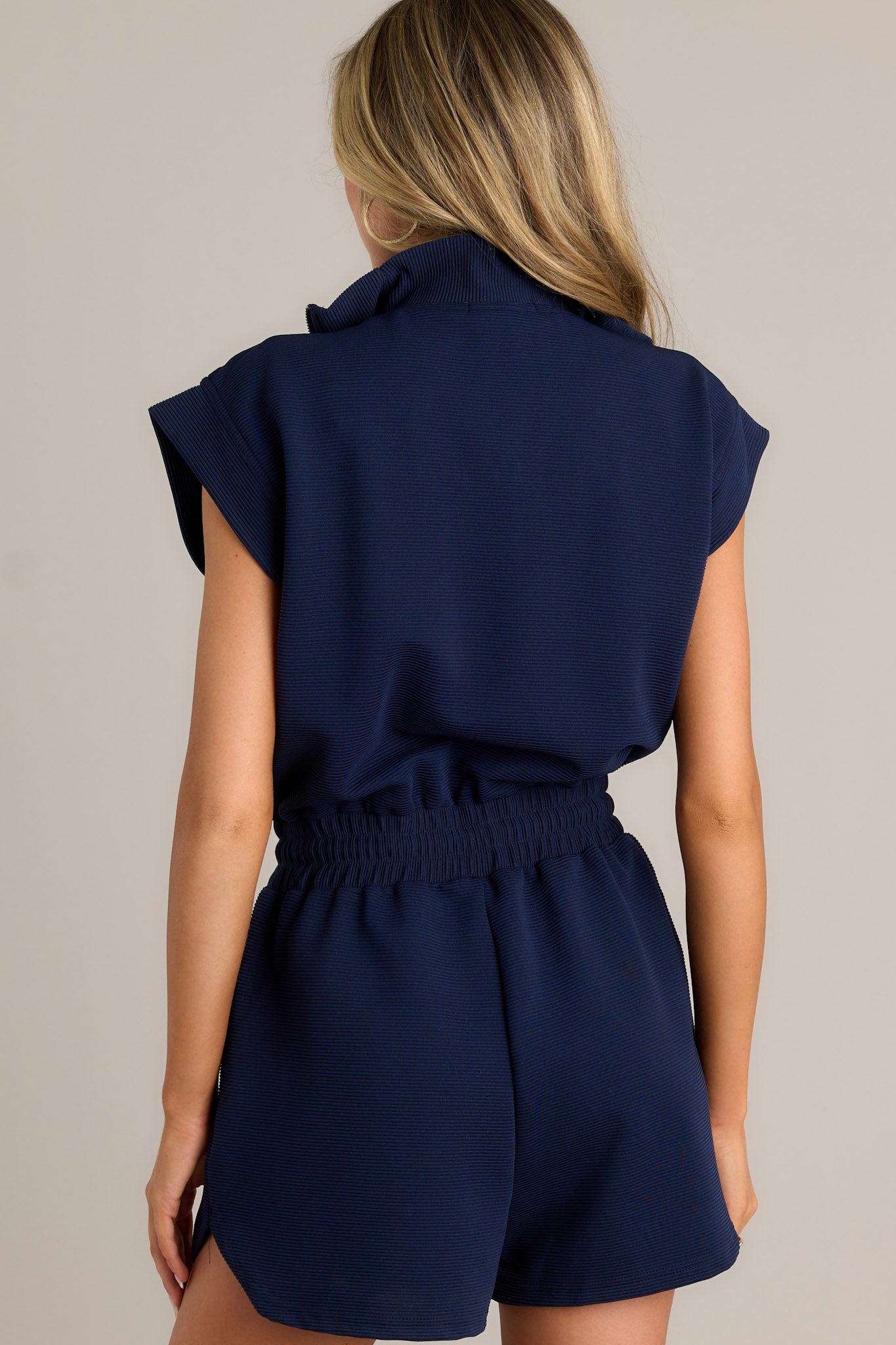 Back view of a navy romper highlighting the overall fit, wide cap sleeves, and ribbed texture.