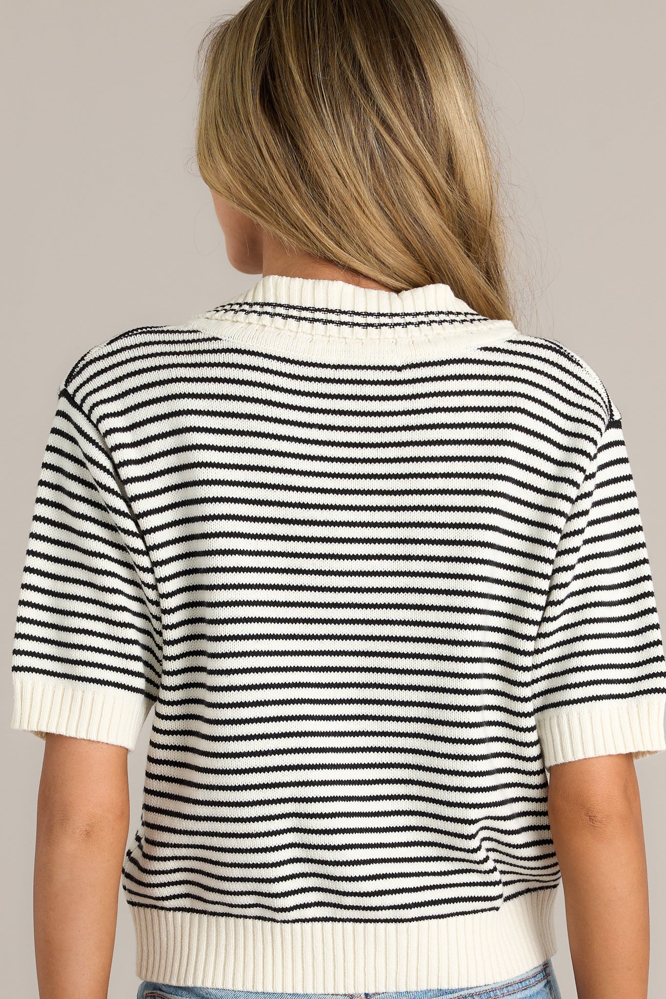 A back view of the sweater, displaying the horizontal striped pattern across the back and the thick hem along the sleeves and bottom edge.