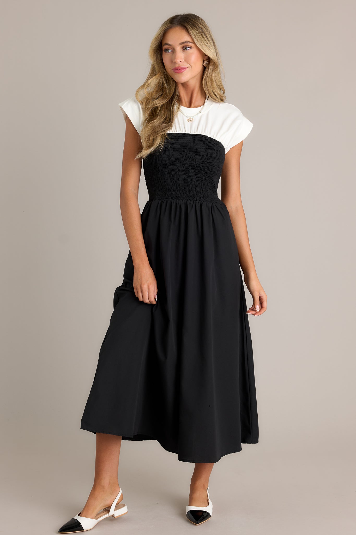 Full length view of a black and white dress with a round neckline, a smocked waist, functional hip pockets, a white color-blocked top, and a flowing silhouette