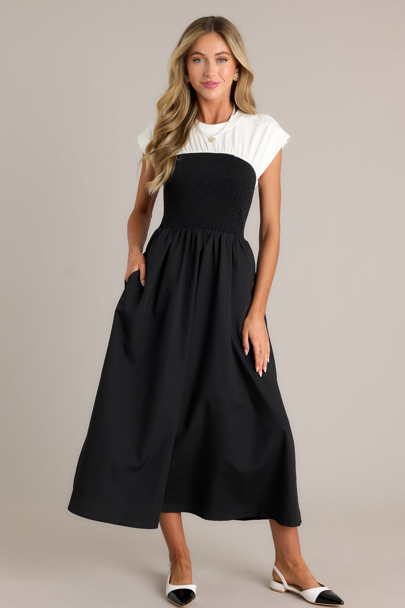 This black and white dress features a round neckline, a smocked waist, functional hip pockets, a white color blocked top and a flowing silhouette.