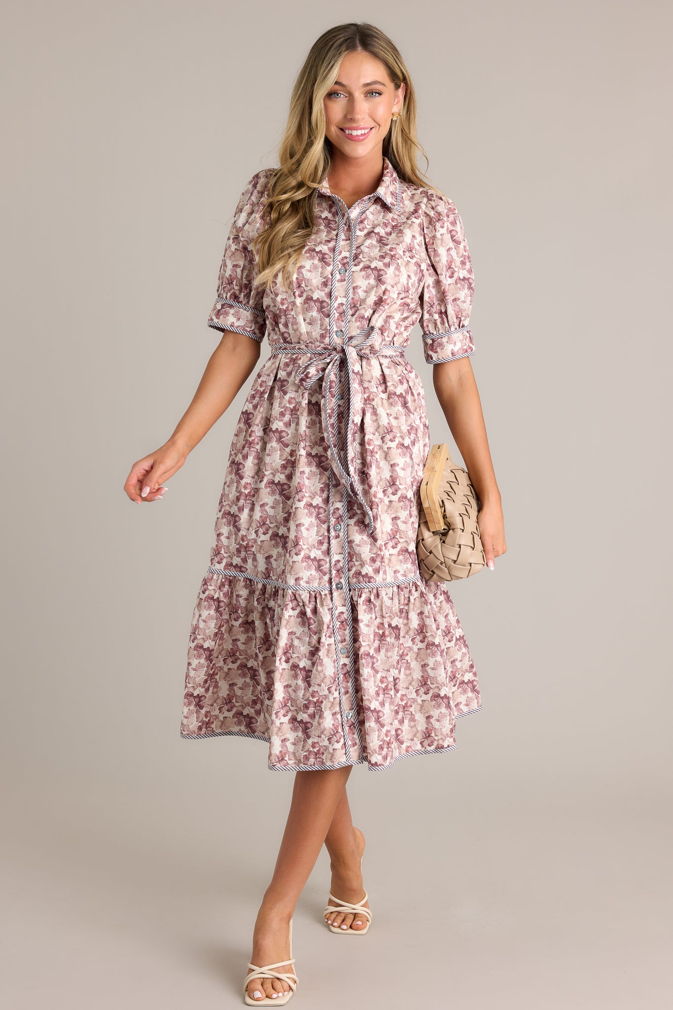 Front angled view of a floral midi dress featuring a collared neckline, a functional button front, functional hip pockets, a self-tie belt on the waist, a tiered design, and puff sleeves