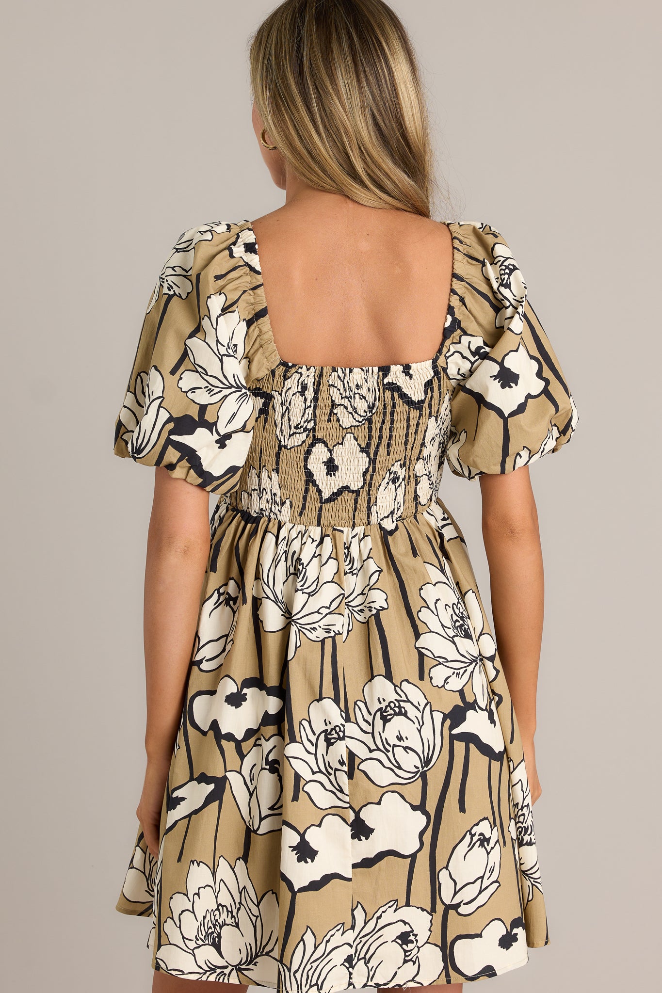 Back view of a taupe mini dress highlighting the fully smocked back, flowing silhouette, and elastic cuffed puff sleeves.