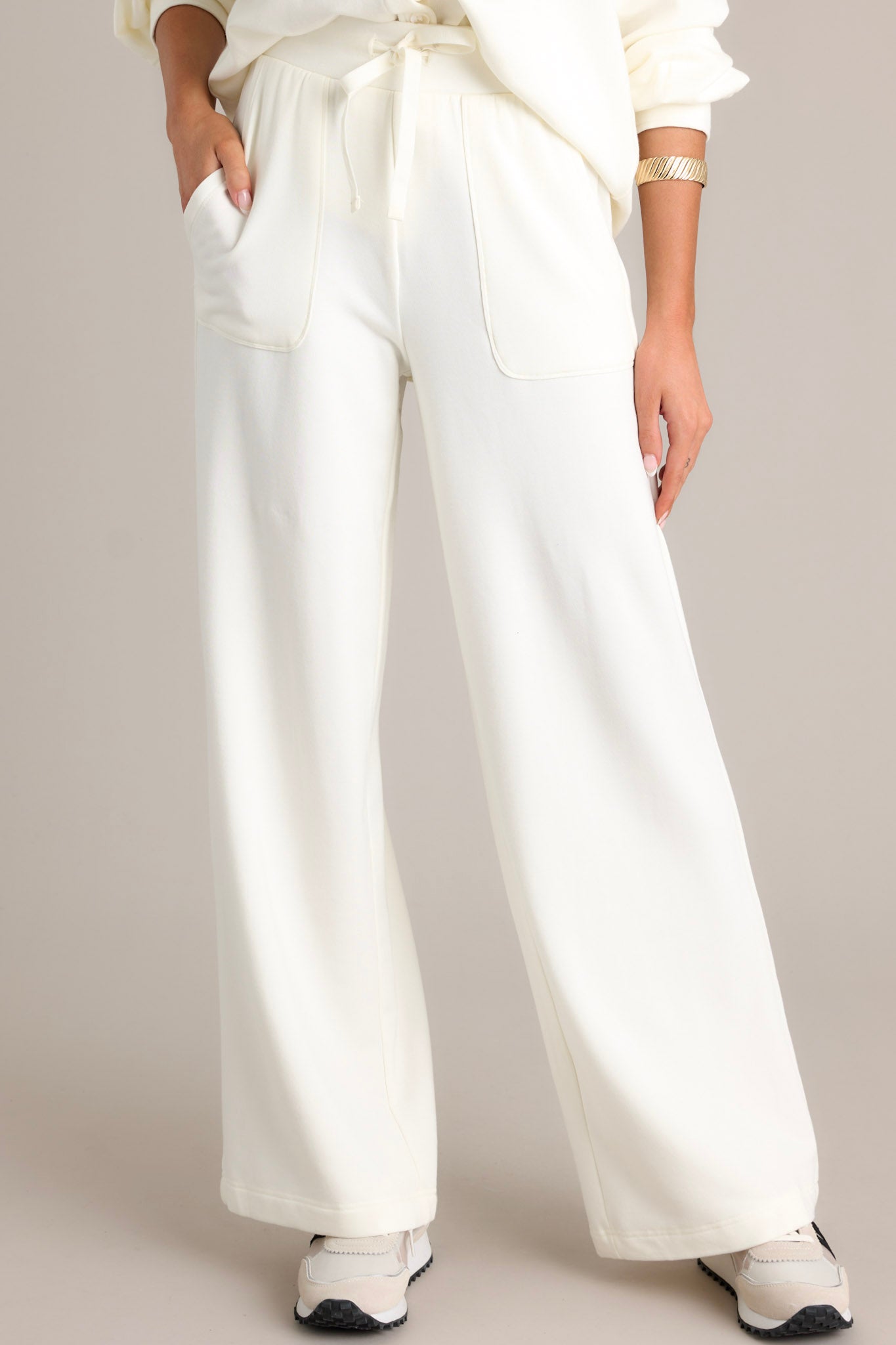 Front angled view of white fleece pants featuring a high waisted design, an elastic waistband with a self-tie drawstring, deep hip pockets, a soft fleece material, and a straight leg