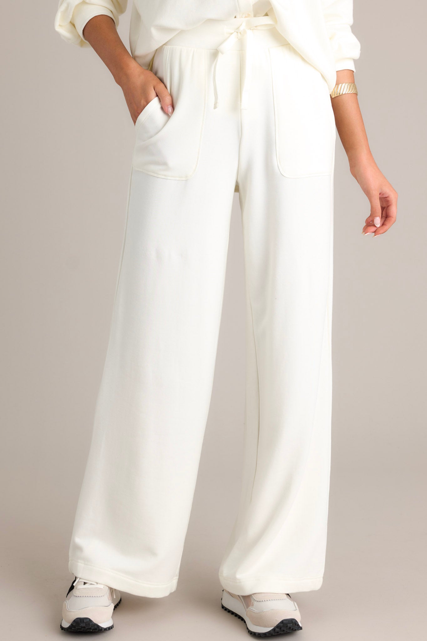 Front view of white fleece pants featuring a high waisted design, an elastic waistband with a self-tie drawstring, deep hip pockets, a soft fleece material, and a straight leg.