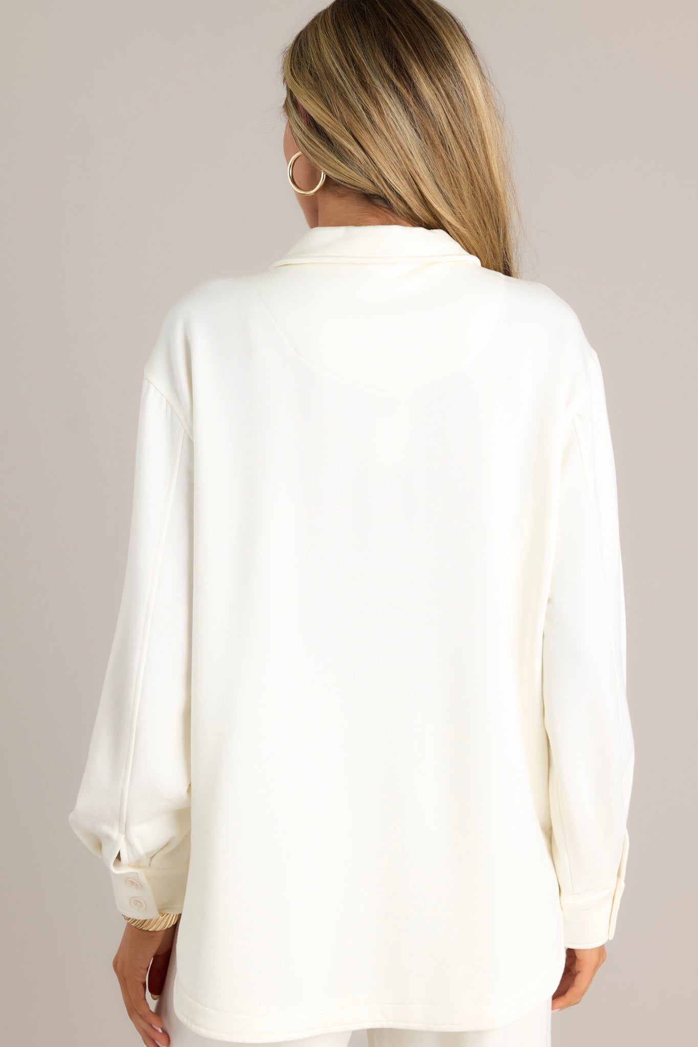 Back view of an ivory button-up highlighting the overall fit, split hemline, and button-cuffed long sleeves.