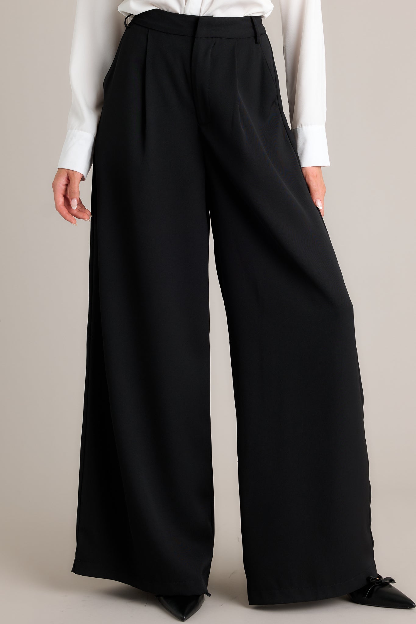 Full length view of black pants featuring a high waist fit, a hook and bar closure, belt loops, pockets, and a wide leg