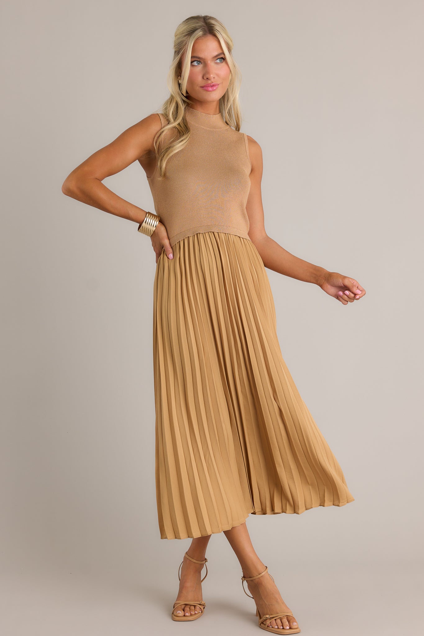 Full body view of this mustard sleeveless dress featuring a high neckline, a ribbed knit bodice, a pleated skirt, a sleeveless design and a flowing silhouette.