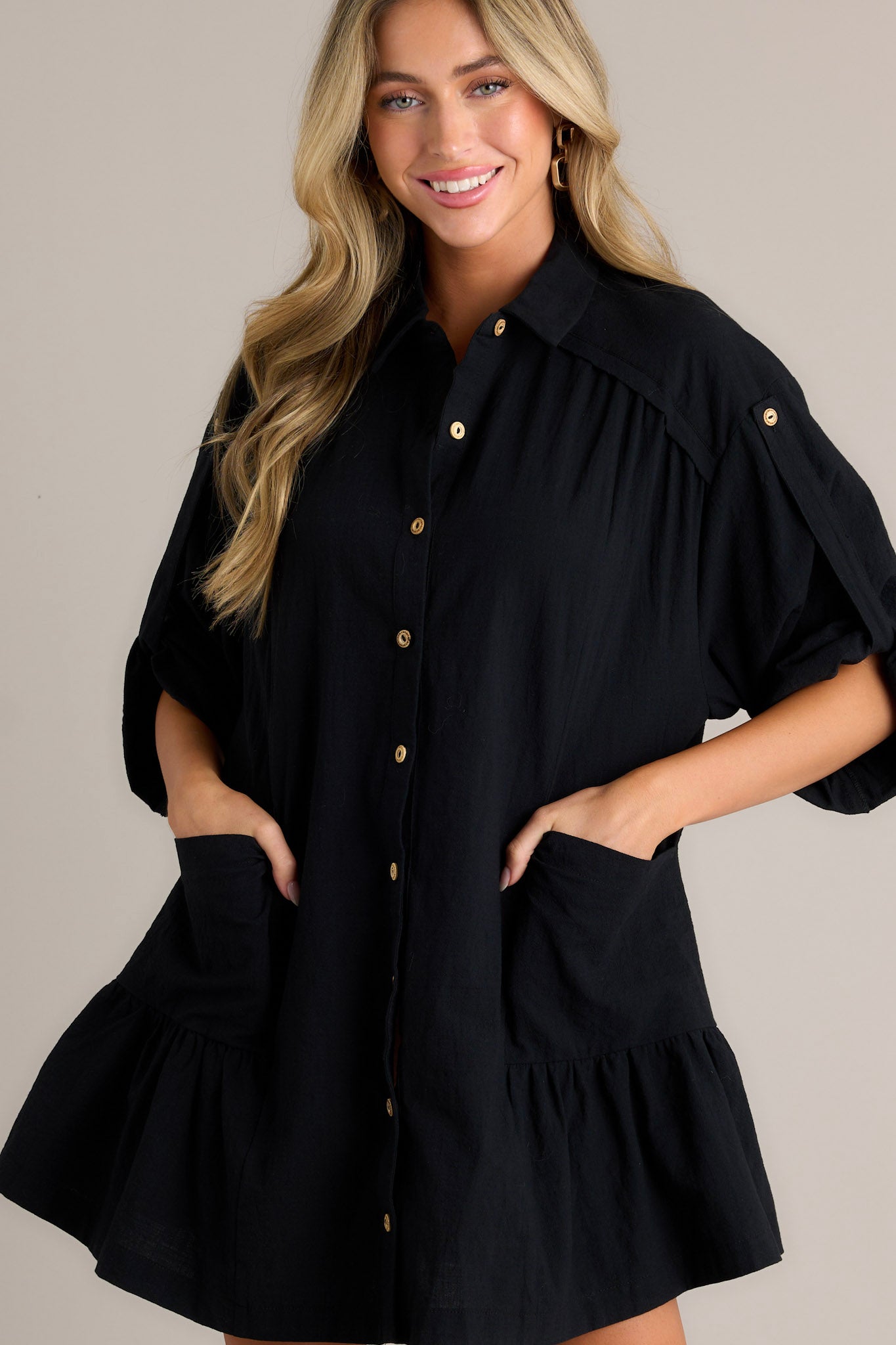 Close-up view of a black dress with a collared high neckline, functional button front, and large front pockets.