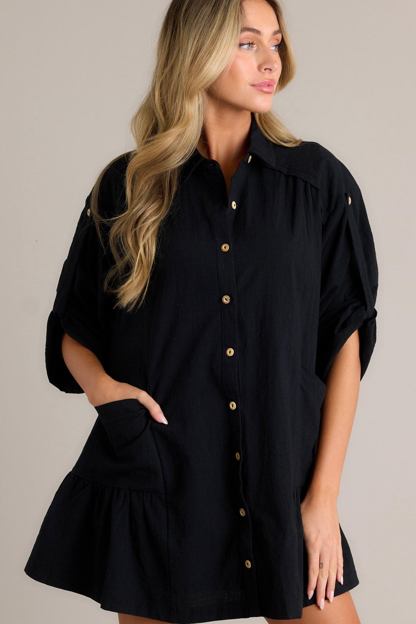 Detailed view of a black dress showcasing its collared high neckline, functional button front, and large front pockets.