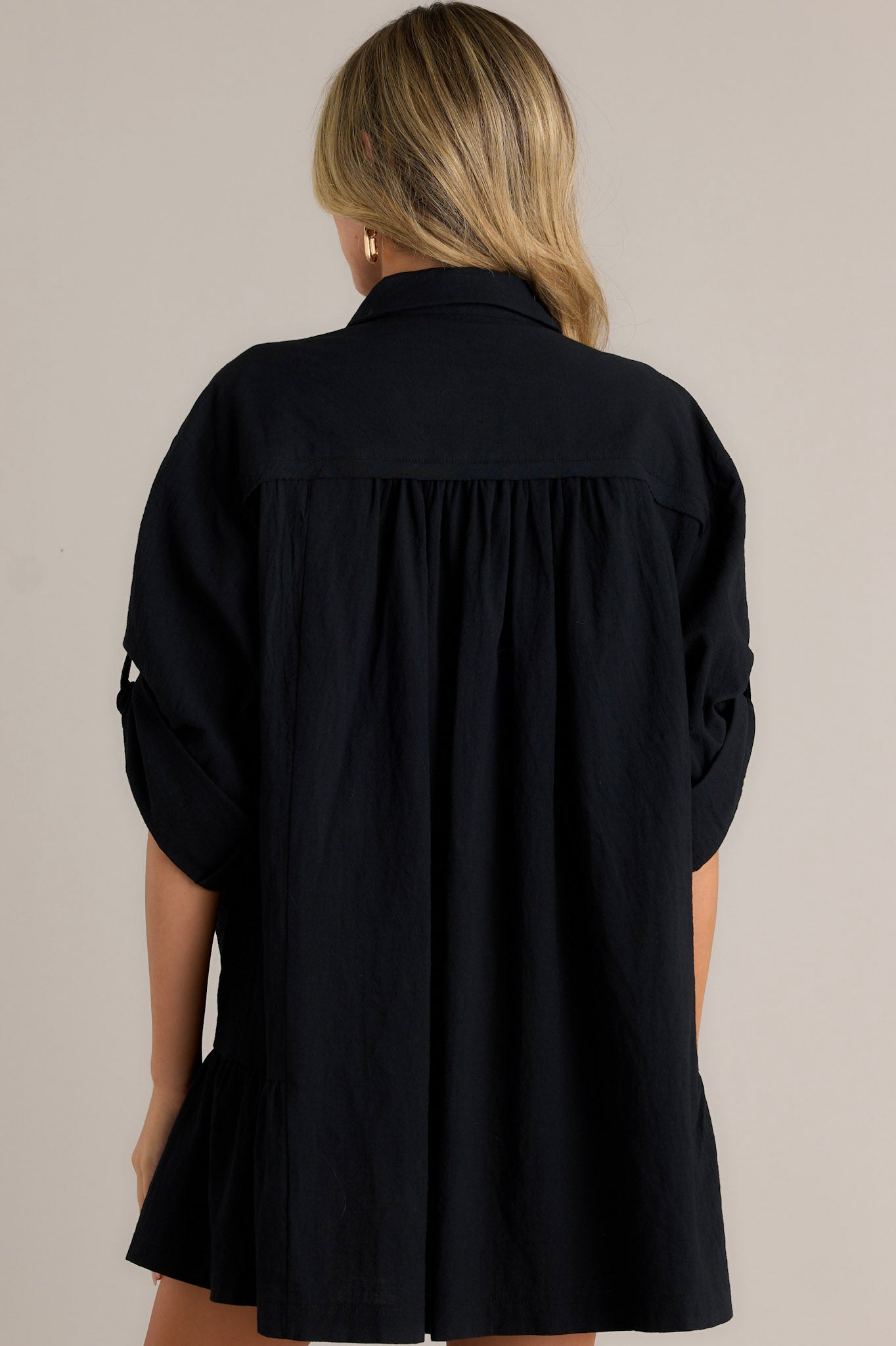 Back view of a black dress with a collared high neckline, loose sleeves, and a ruffled hem.