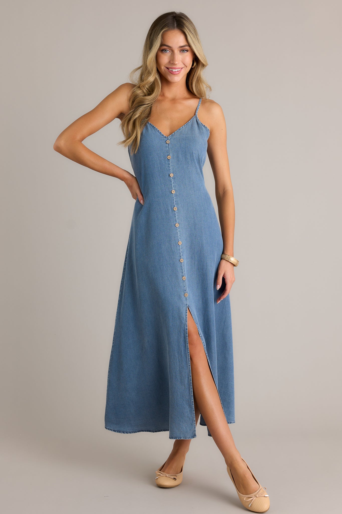 Full length view of a chambray maxi dress with a v-neckline, button front design, smocked back insert, adjustable spaghetti straps, and an open leg slit,