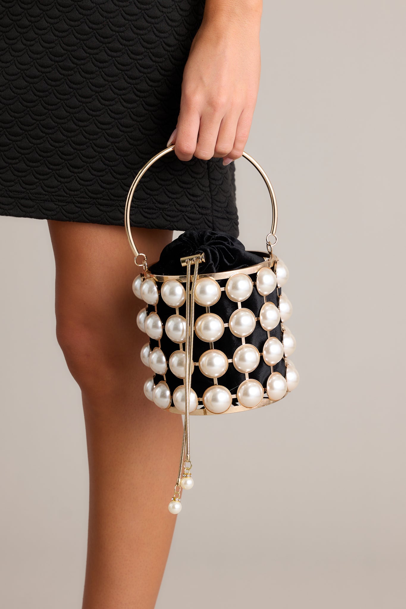 Front view of this clutch featuring a cylindrical shape, large faux pearls, a gold drawstring, a gold handle and gold accents around the faux pearls.