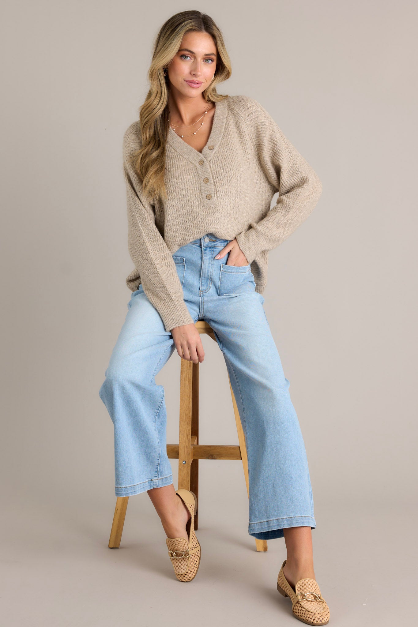 Seated Front view of a sweater featuring a v-neckline, functional buttons down the front, ribbed detailing throughout, and ribbed ruffled long sleeves.