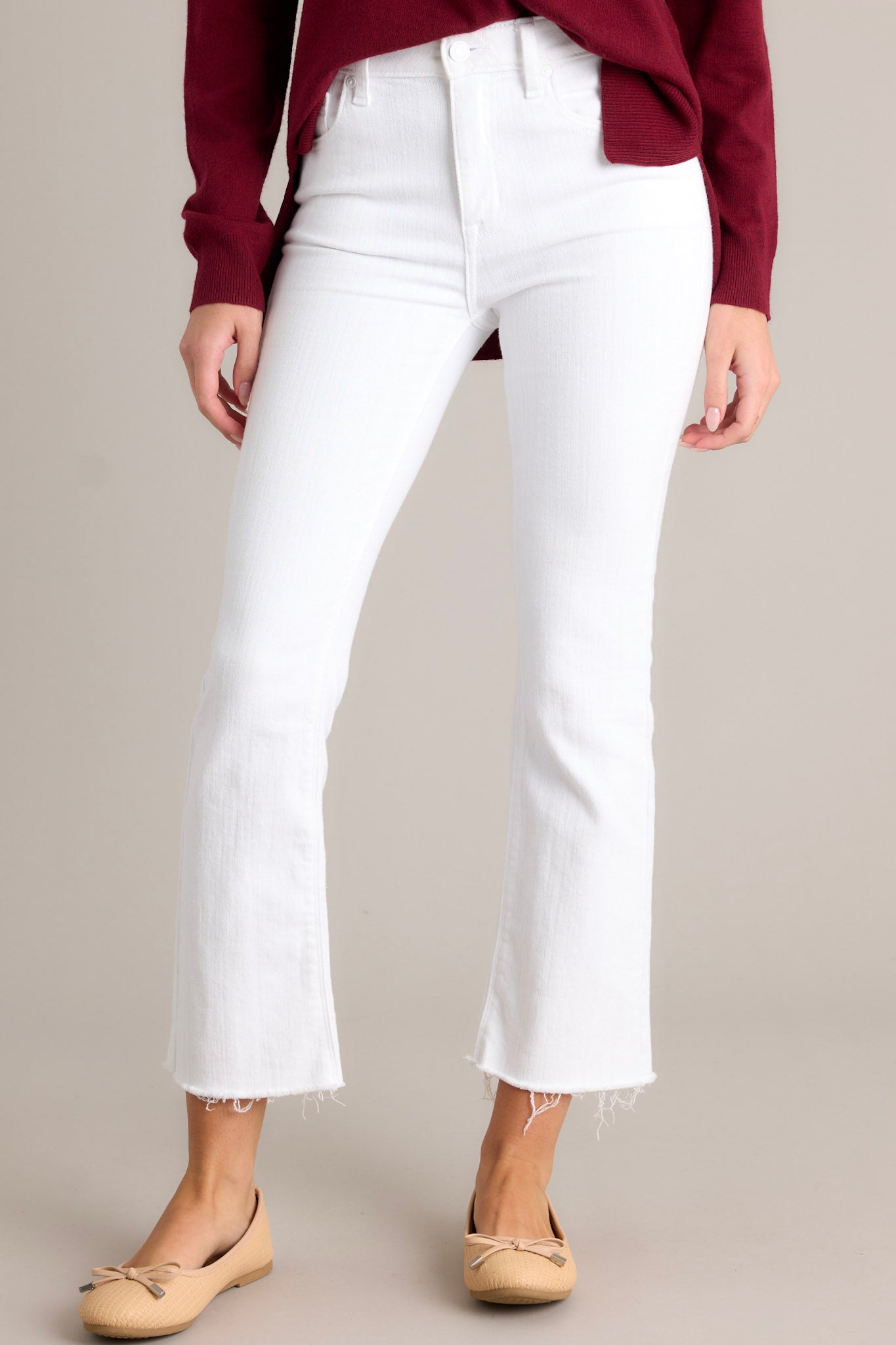 Front  view of these white jeans that feature a high waisted design, a classic button & zipper closure, belt loops, functional front & back pockets, and a raw, cropped hemline.