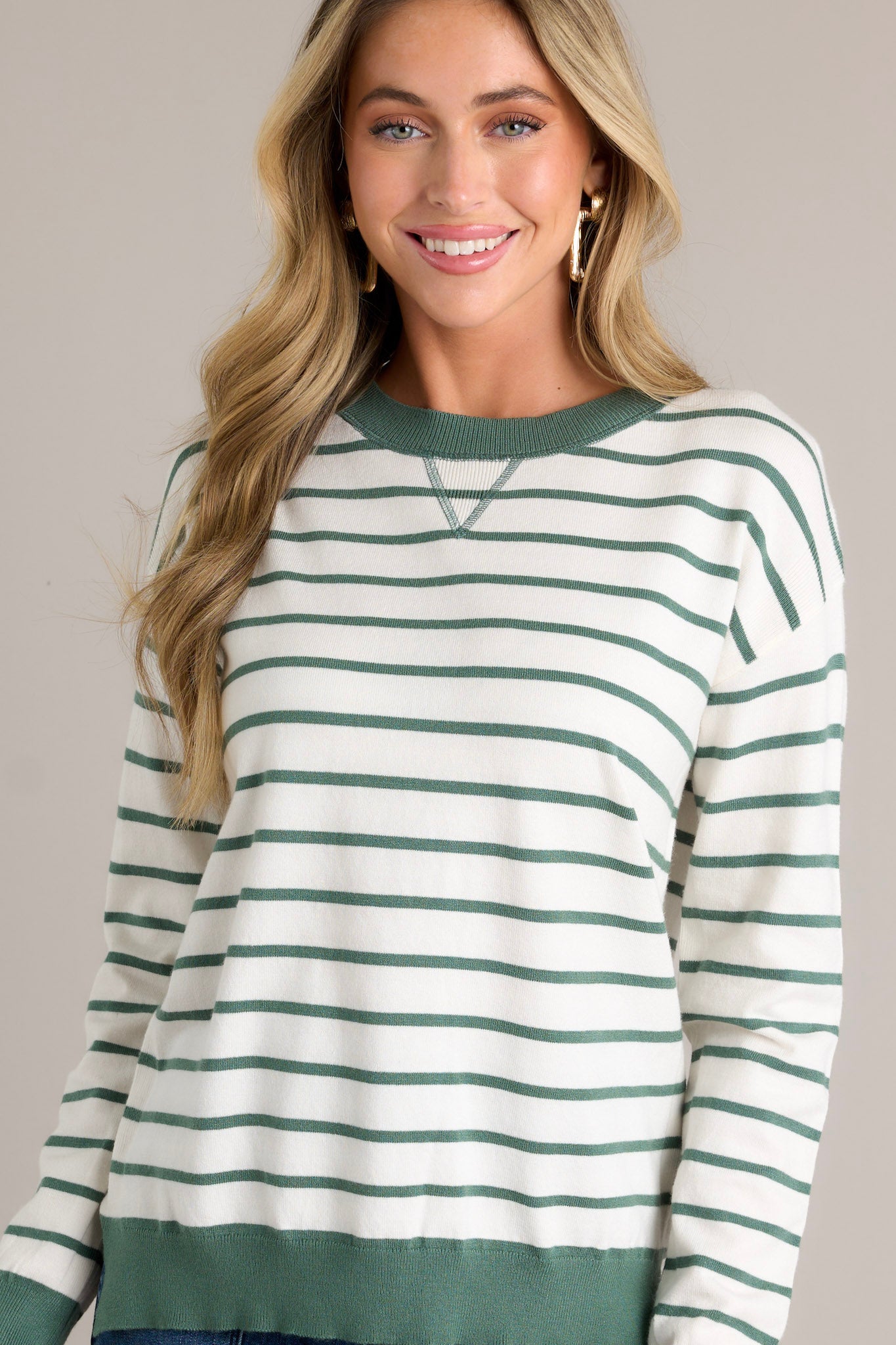 Front view of a striped long sleeve top featuring a rounded neckline, a green horizontal stripe design, green trim, long cuffed sleeves, and a thick hem with side slits.