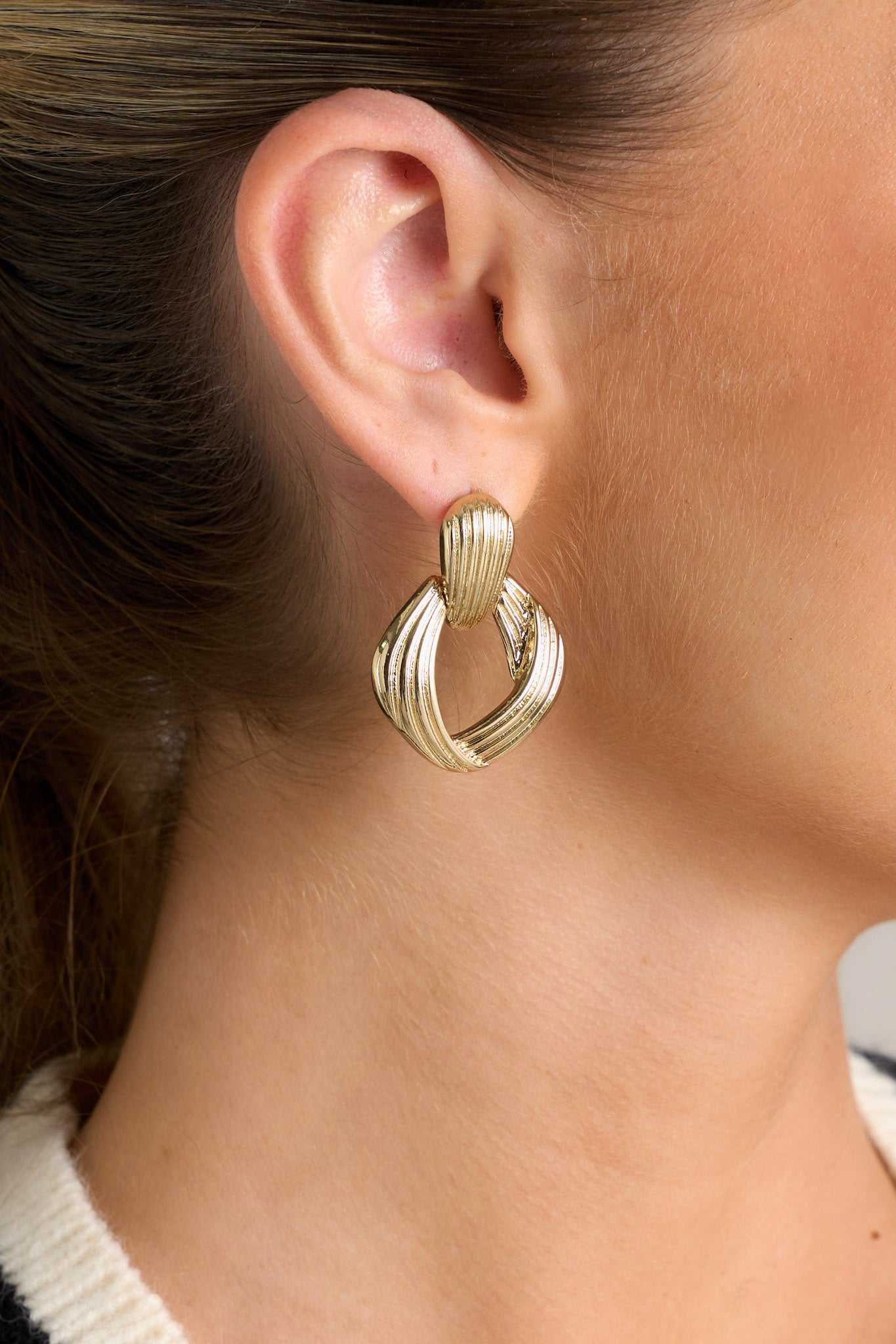 Close-up view of these earrings feature a ribbed stud with a connected ribbed diamond shaped hoop with the ribs increasing in size in the hoop.