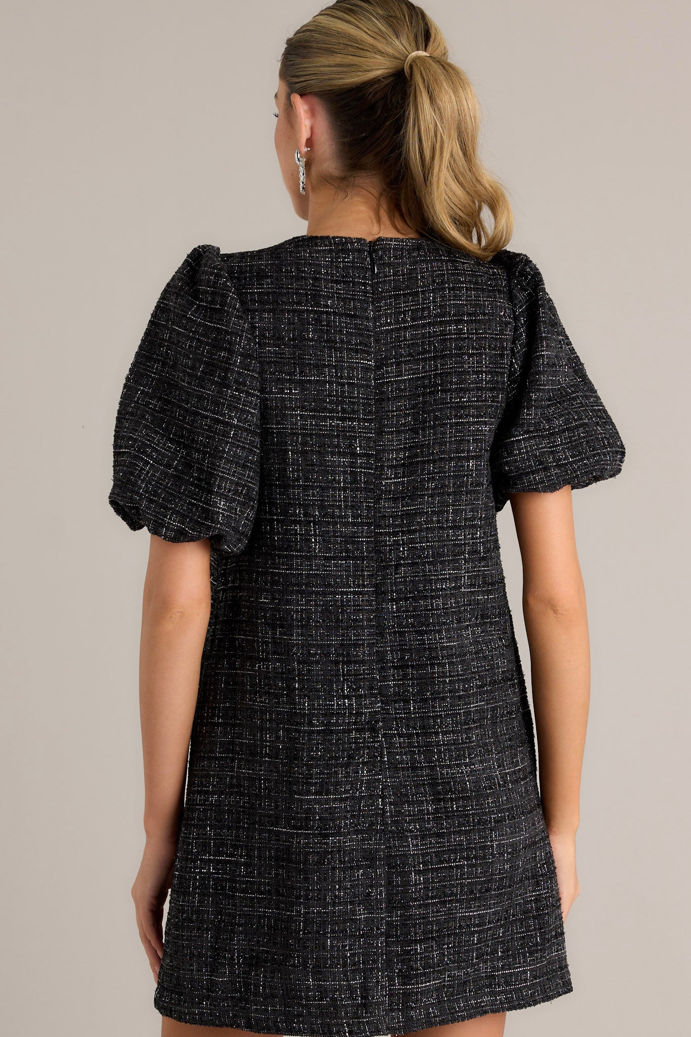 Back view of a black tweed dress with short puff sleeves and a round neckline.