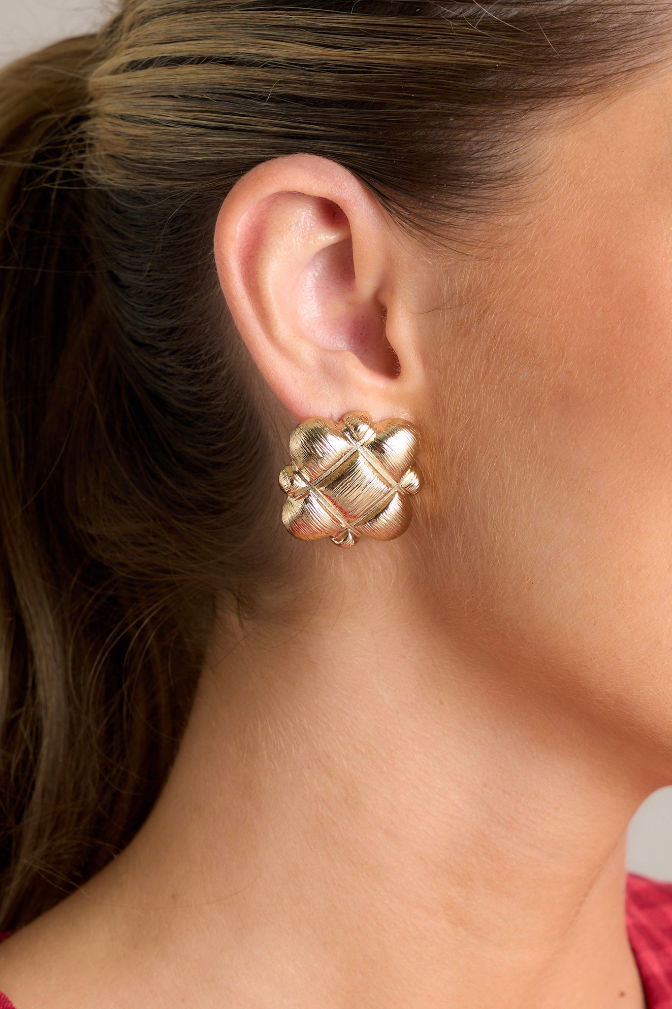 Close-up view of these gold earrings feature a geometric pattern with a square in the middle surrounded with semi-circles, a gold textured design and secure post backings.