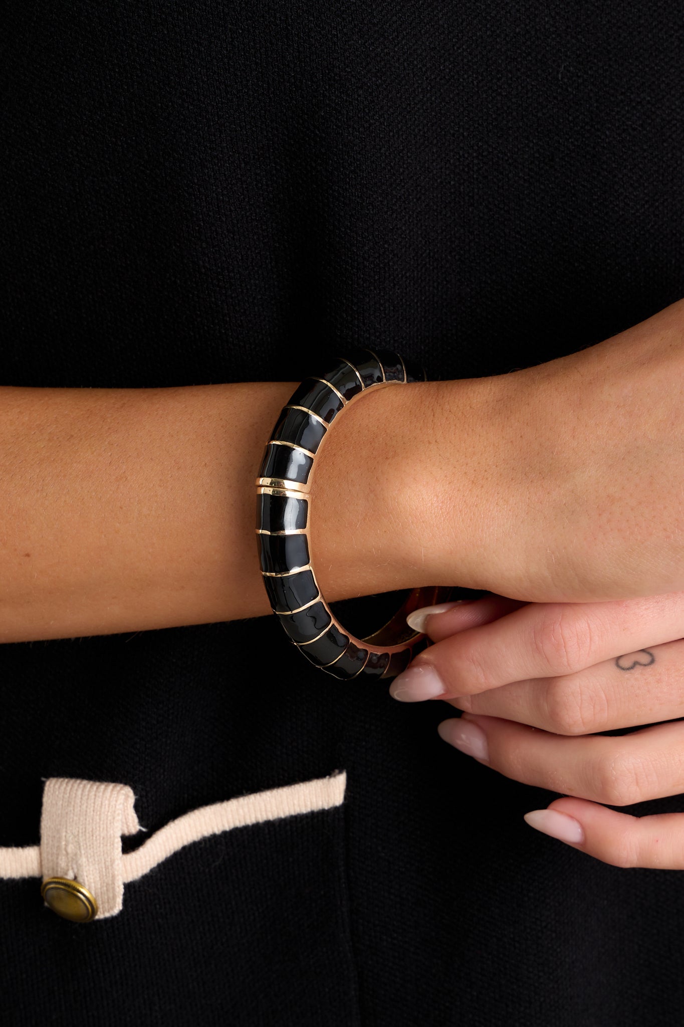 This hinged bracelet features a black and gold pattern, a gold inside, and a hinge closure.