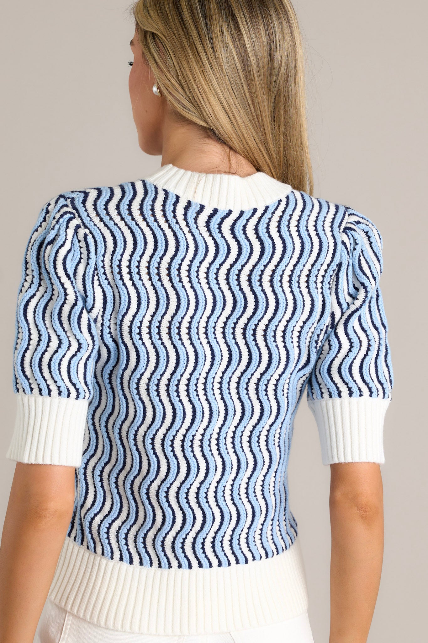 Back view of a blue stripe sweater top highlighting the wavy blue and white stripe design, thick hemline, and short sleeves.